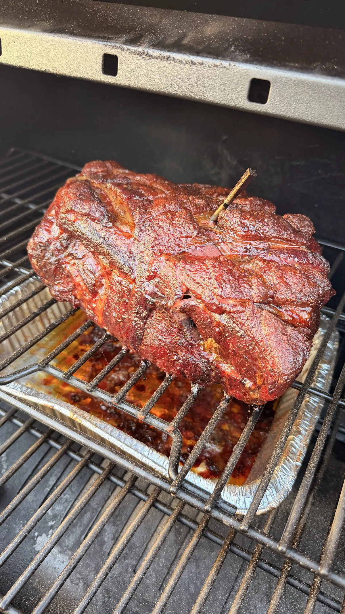 Bone-in pork butt coated in sweet BBQ rub developing bark in smoker at 250°F