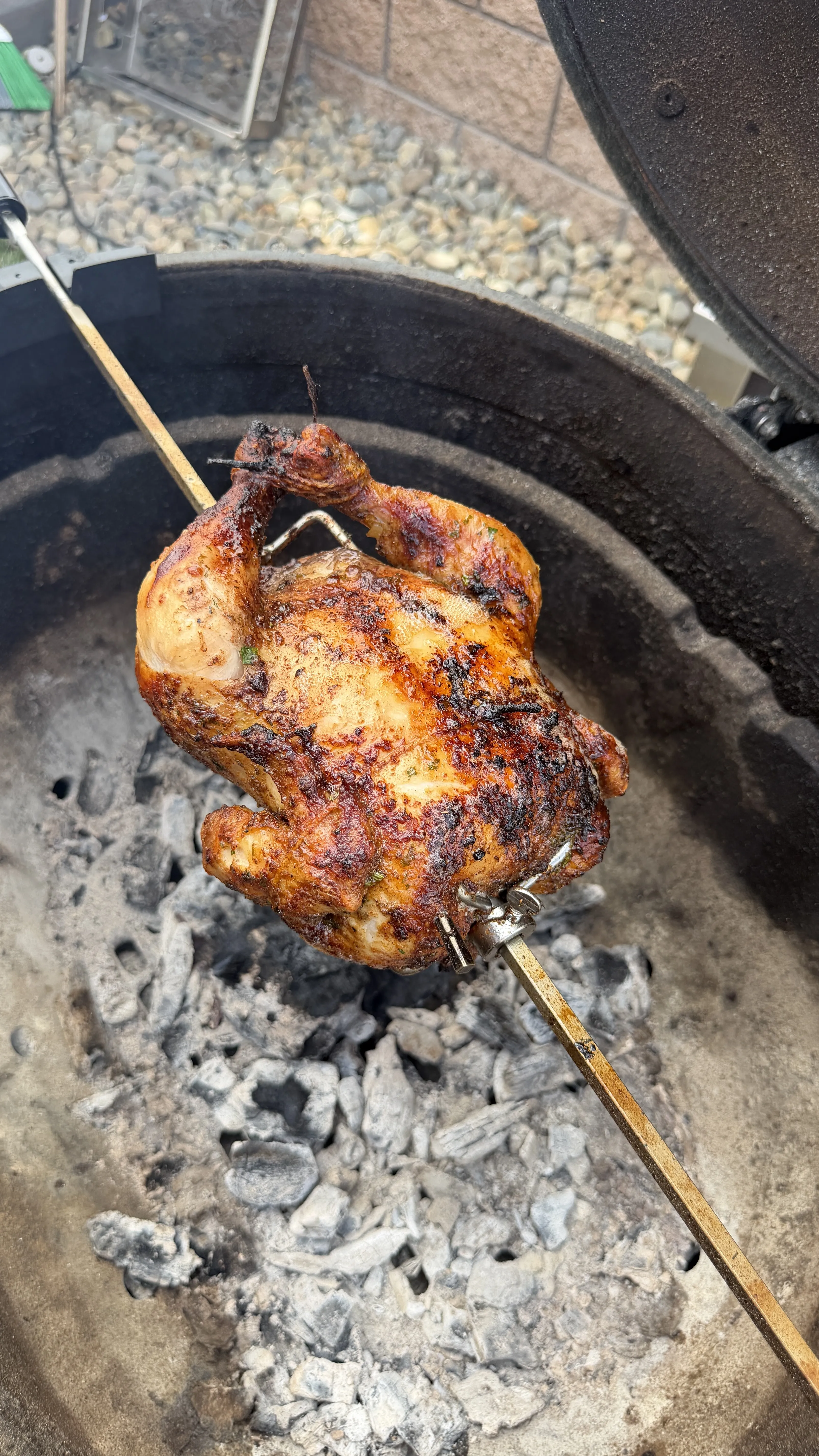 Whole Cajun butter rotisserie chicken on a spit over charcoal in a kettle grill, with golden-brown crispy skin