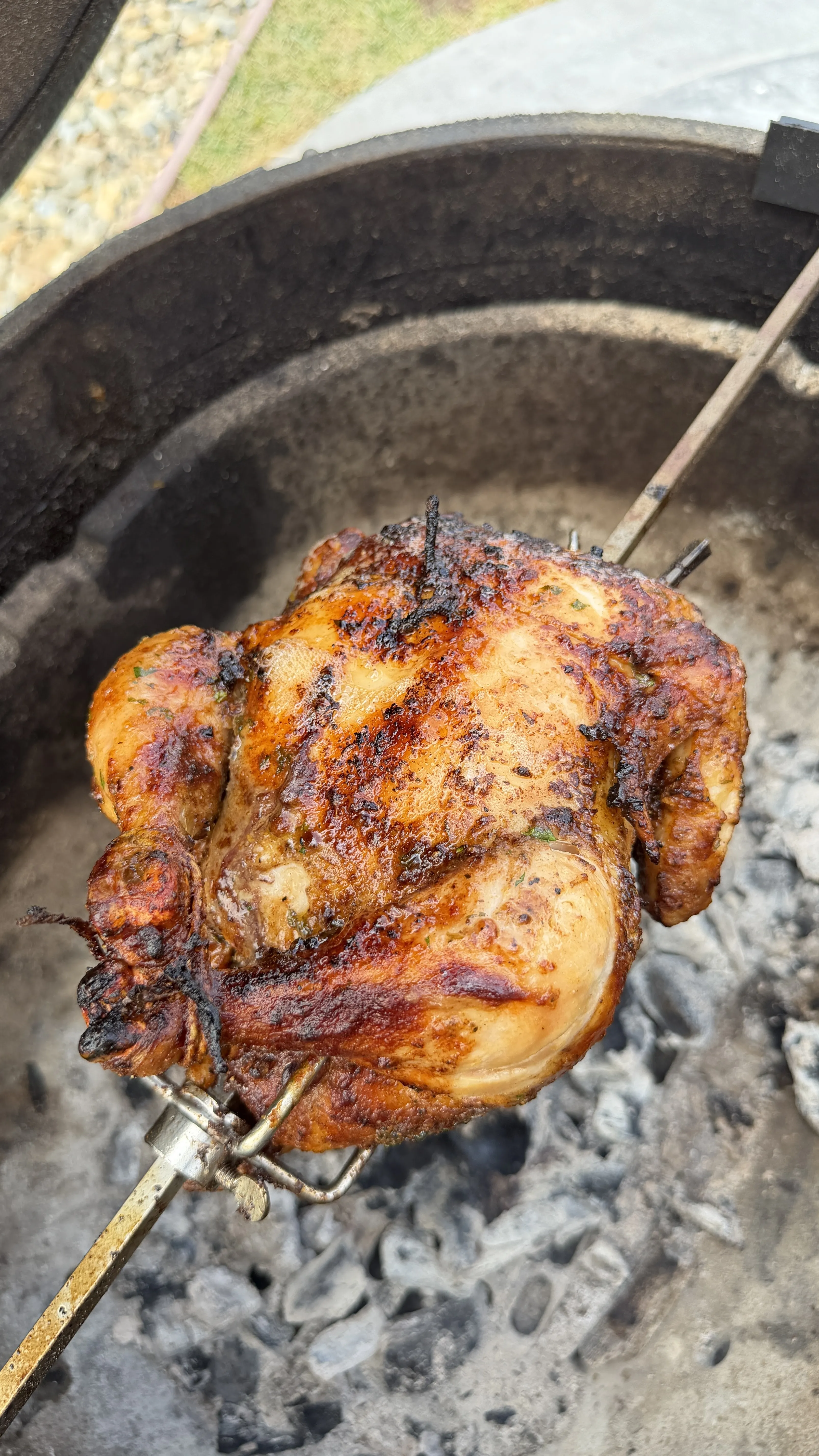 Whole Cajun butter rotisserie chicken on a spit over charcoal, with golden-brown crispy skin and charred spices