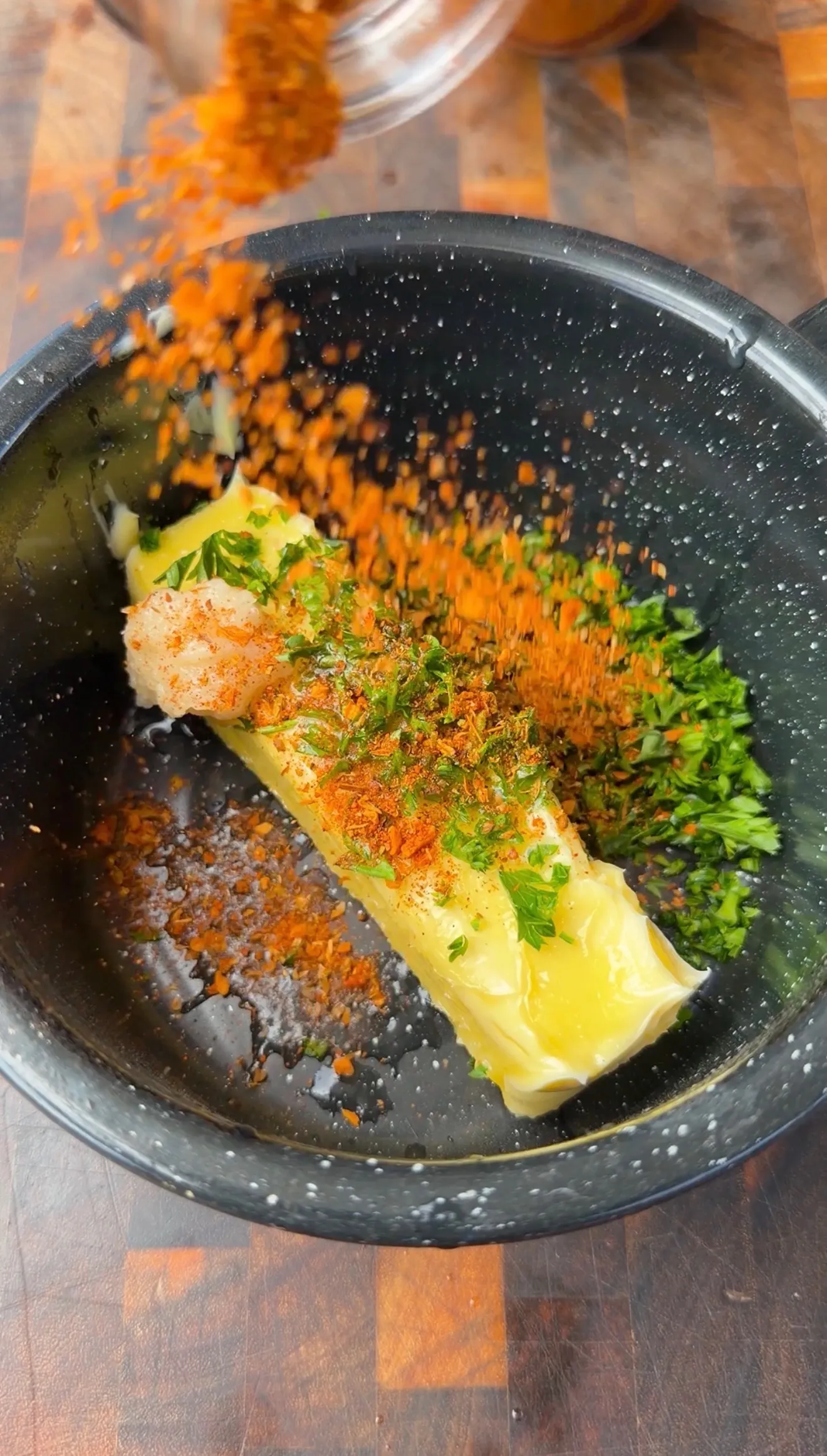 Stick of butter with Cajun spices, fresh parsley, and garlic being combined in a dark mixing bowl