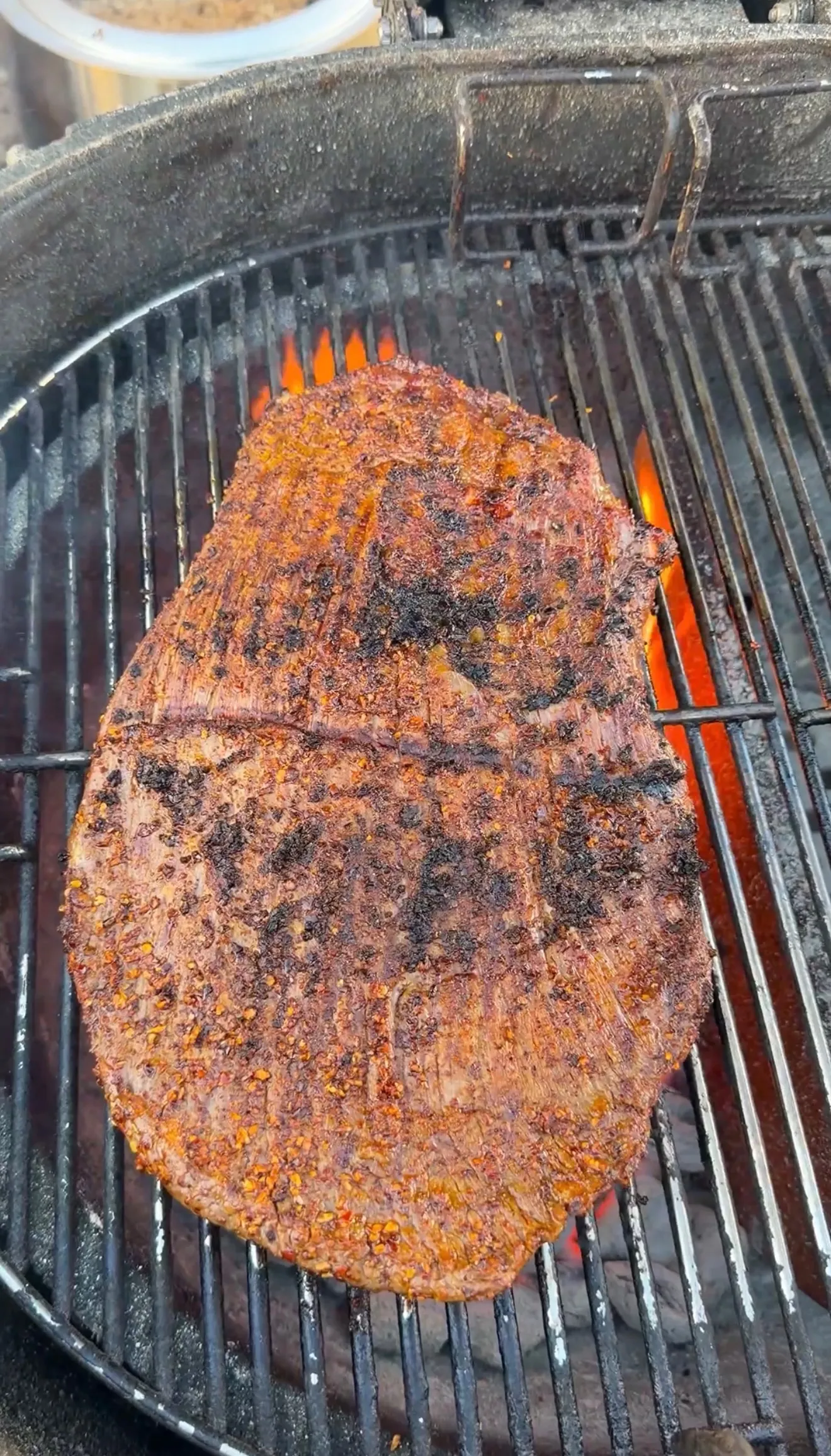Seasoned carne asada steak with spice rub grilling over hot charcoal flames on a round grill