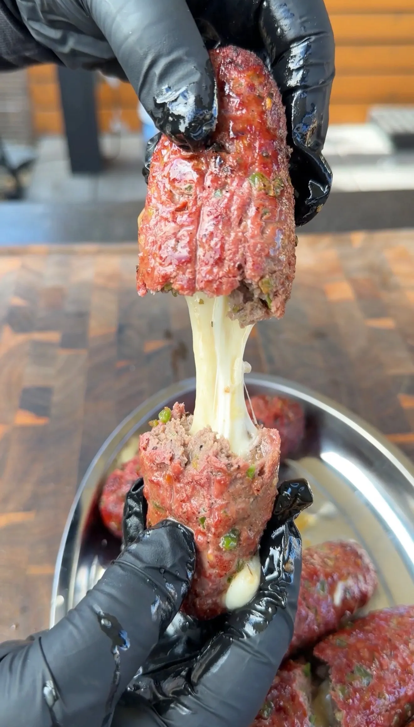 Cheese stuffed burger dog being pulled apart revealing gooey melted cheese stretch, held with black gloves