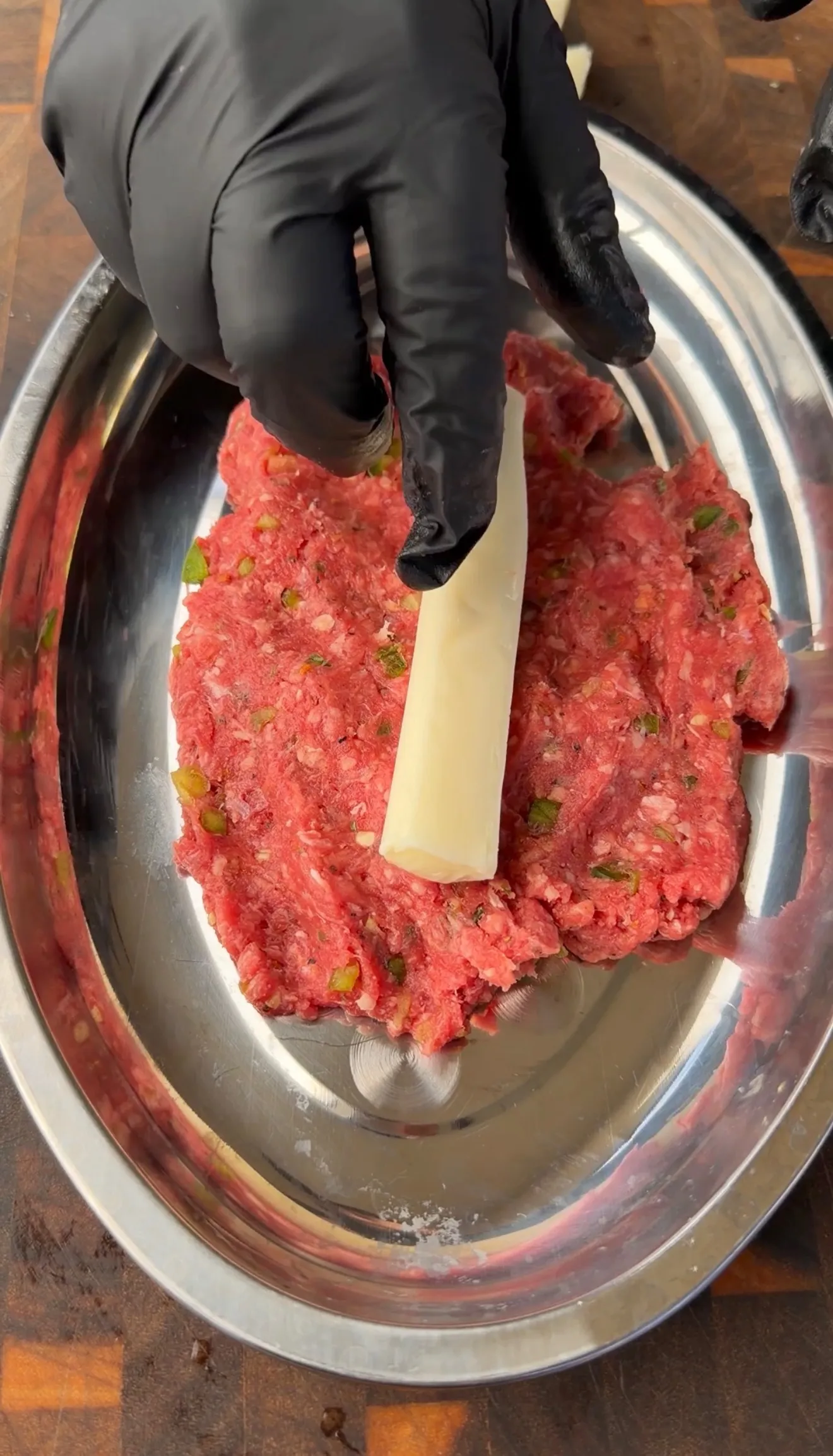 Hands in black gloves placing a mozzarella cheese stick into seasoned ground beef for cheese stuffed burger dogs