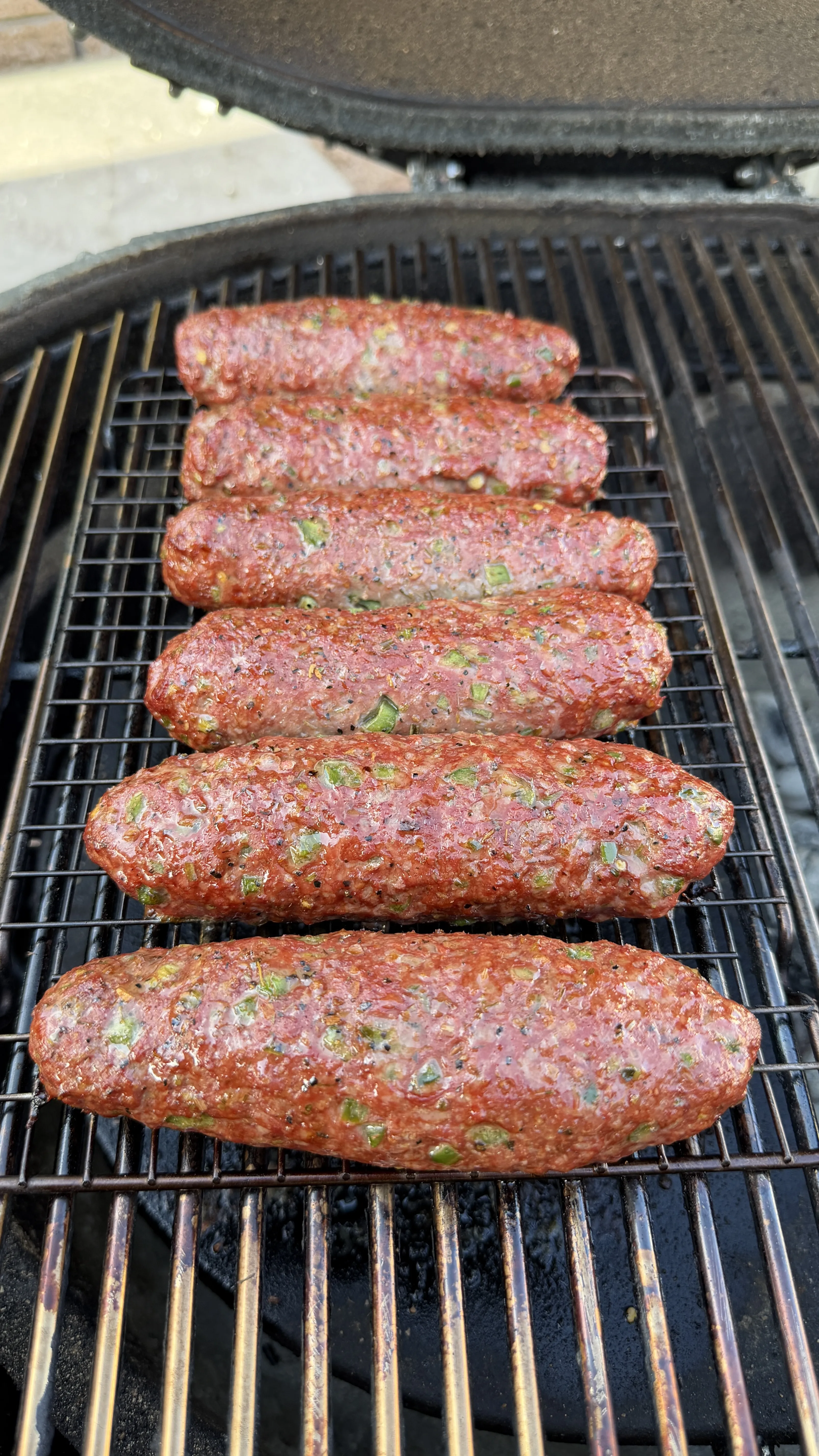 Raw cheese stuffed burger dogs shaped like sausages on a charcoal grill grate