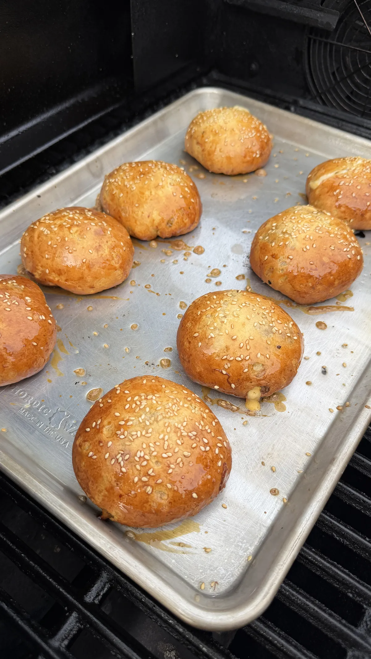 Golden baked cheeseburger bombs topped with sesame seeds on a silver sheet pan on a grill