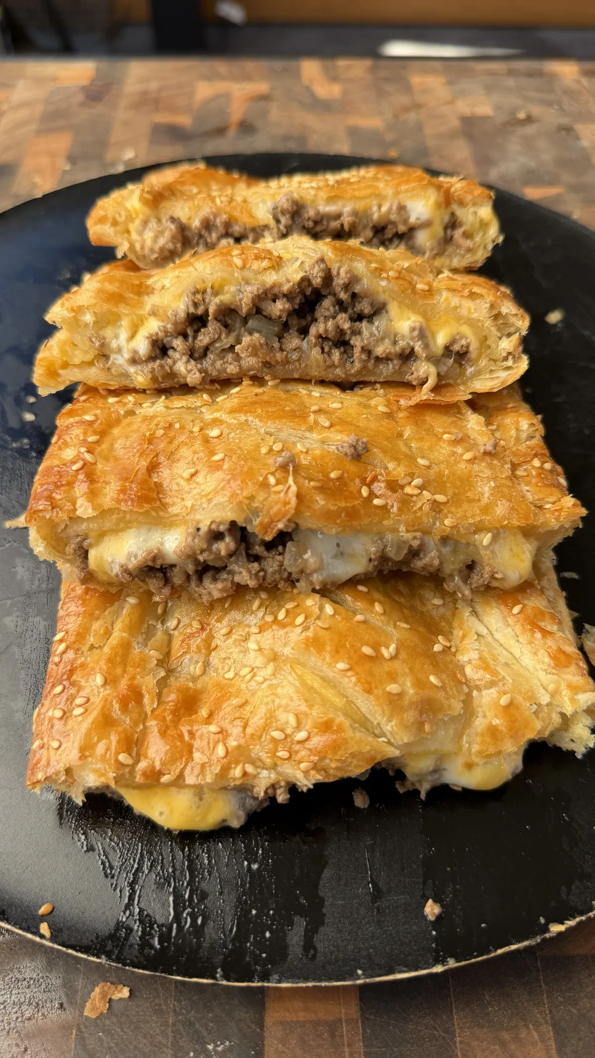 Sliced homemade cheeseburger hot pockets made with golden puff pastry, sesame seeds, melted cheese, and seasoned ground beef filling