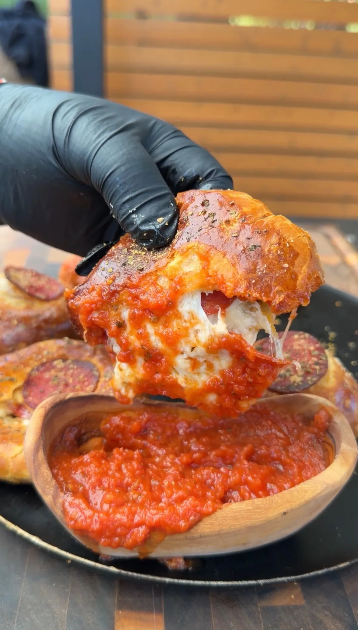 A gloved hand pulling apart a cheesy pizza bomb over marinara dipping sauce, with melted mozzarella stretching