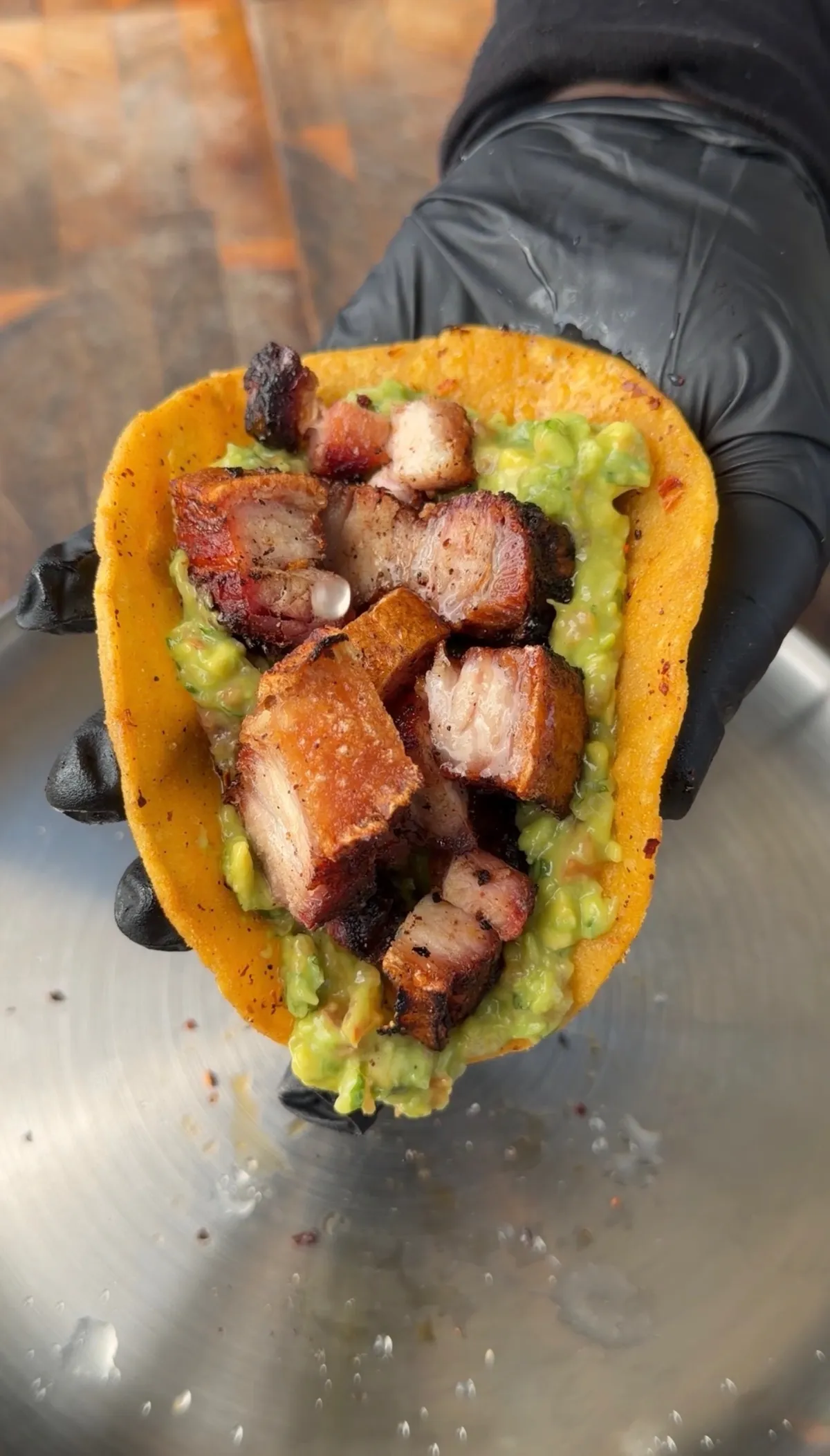 Hand holding a corn tortilla taco filled with crispy chicharron chunks and creamy guacamole