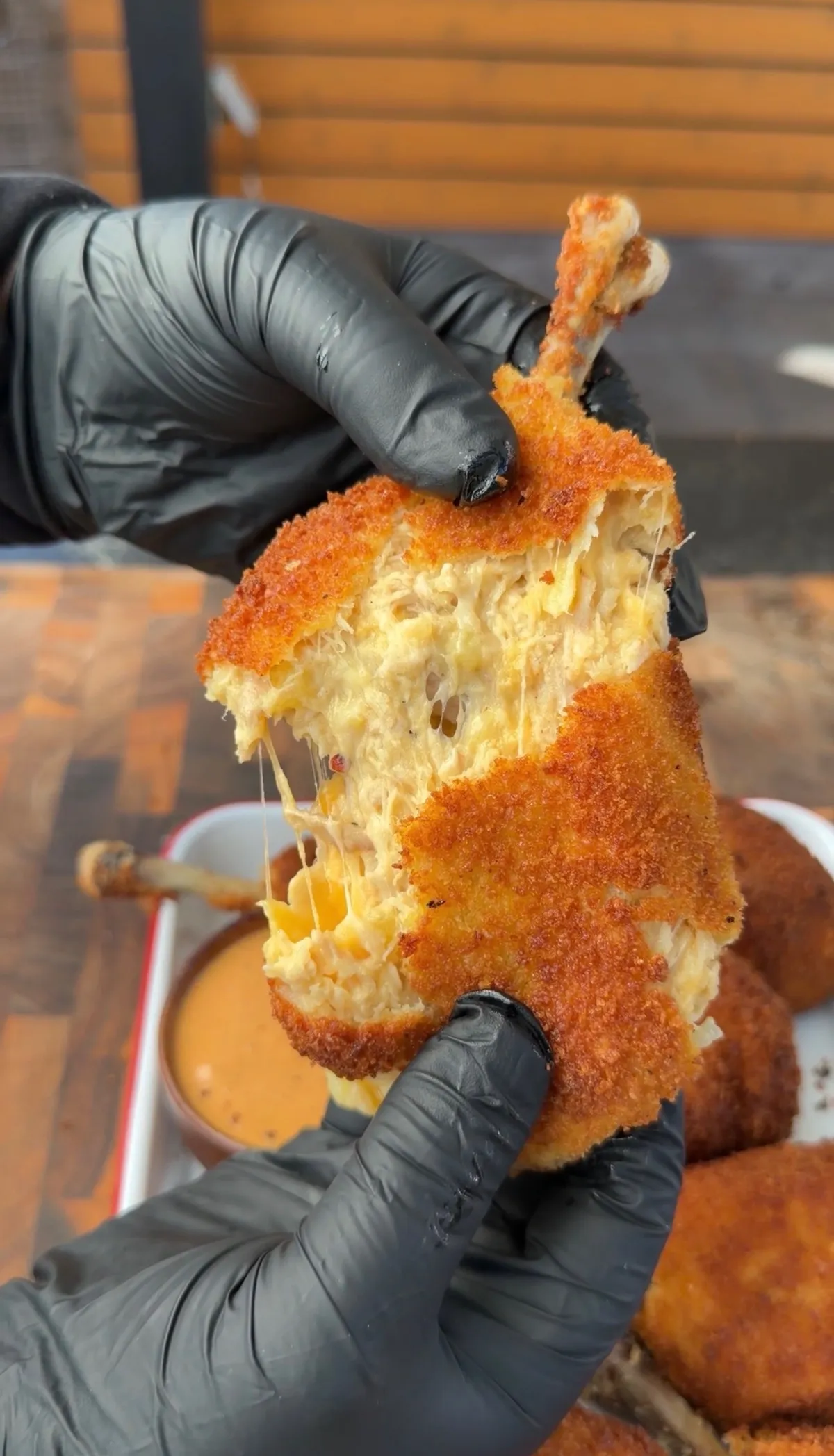 Hands pulling apart a fried chicken potato cheese bomb on a bone, revealing shredded chicken, mashed potato, and melted cheese inside