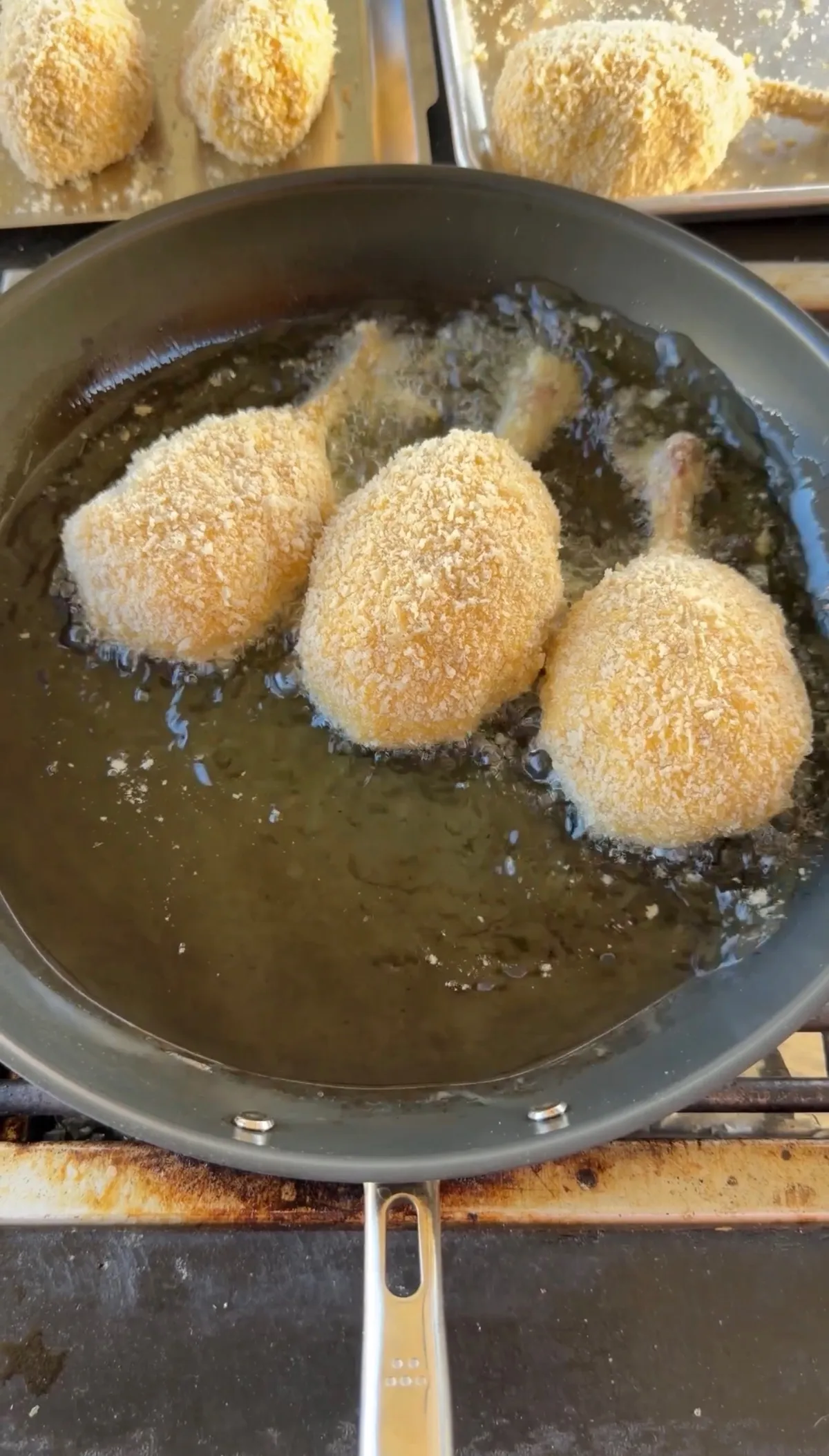 Three panko-breaded chicken potato cheese bombs on bones frying in hot oil in a skillet until golden and crispy