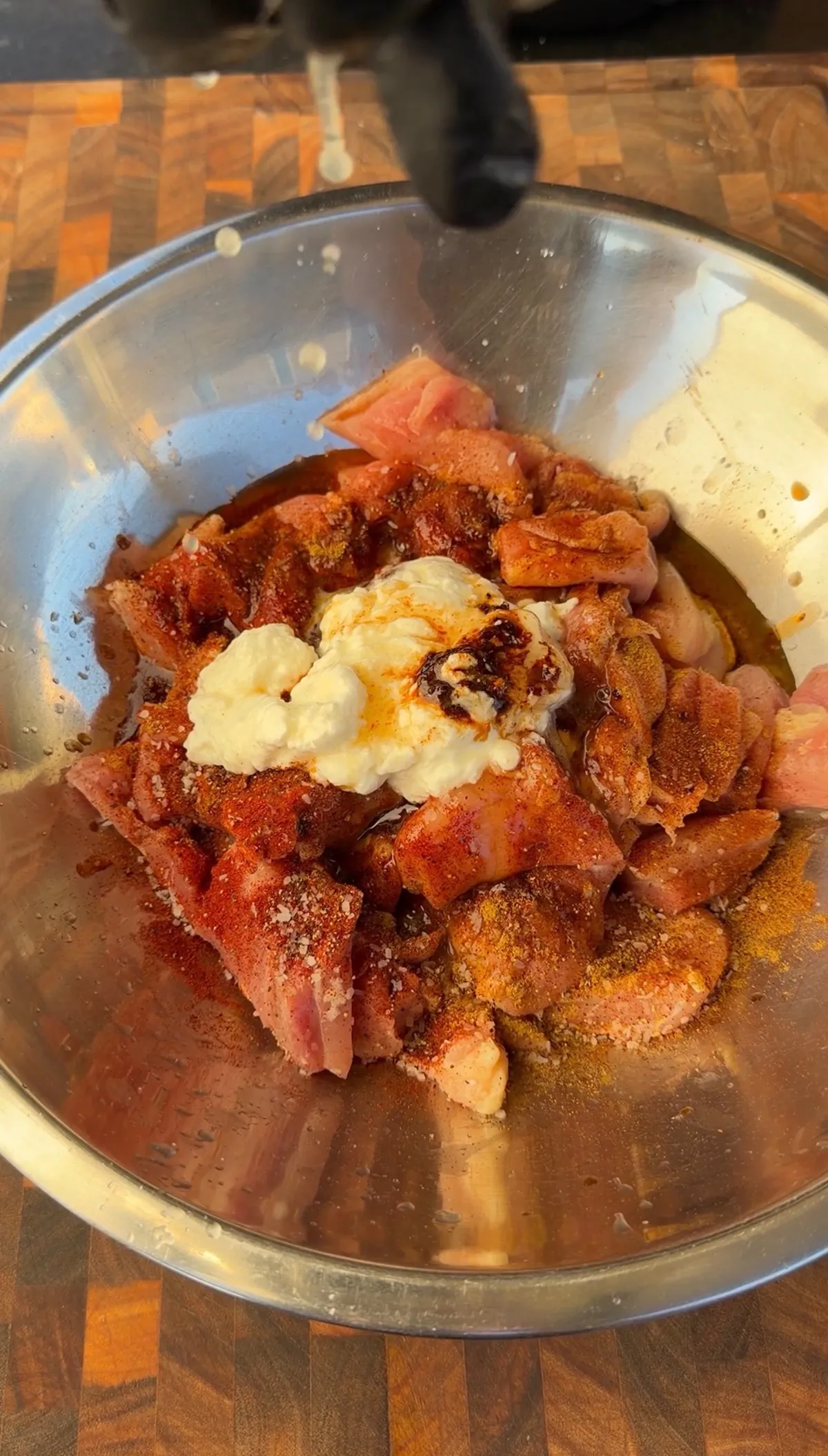 Bite-size chicken thigh pieces in a steel bowl with Greek yogurt, smoked paprika, cumin, and chili powder marinade