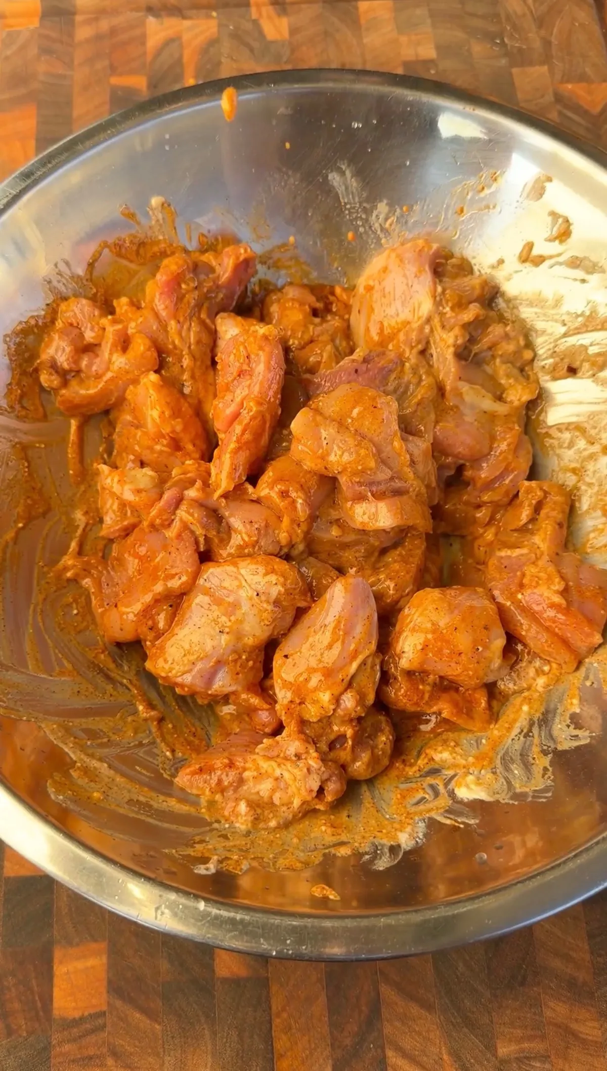 Raw chicken thigh pieces coated in chili-lime marinade with smoked paprika, cumin, and Greek yogurt in a steel bowl