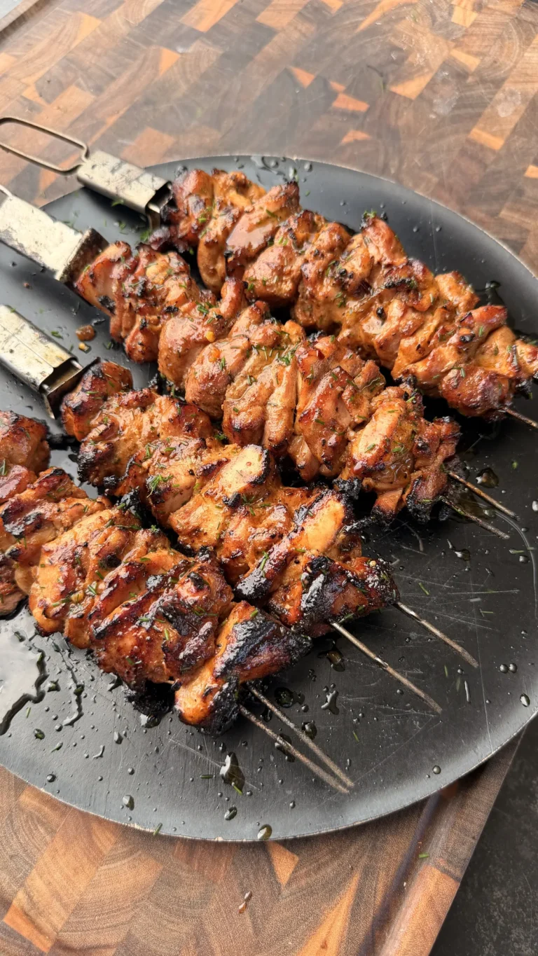 Grilled chili-lime chicken thigh skewers with chili crisp glaze and fresh cilantro on a dark plate