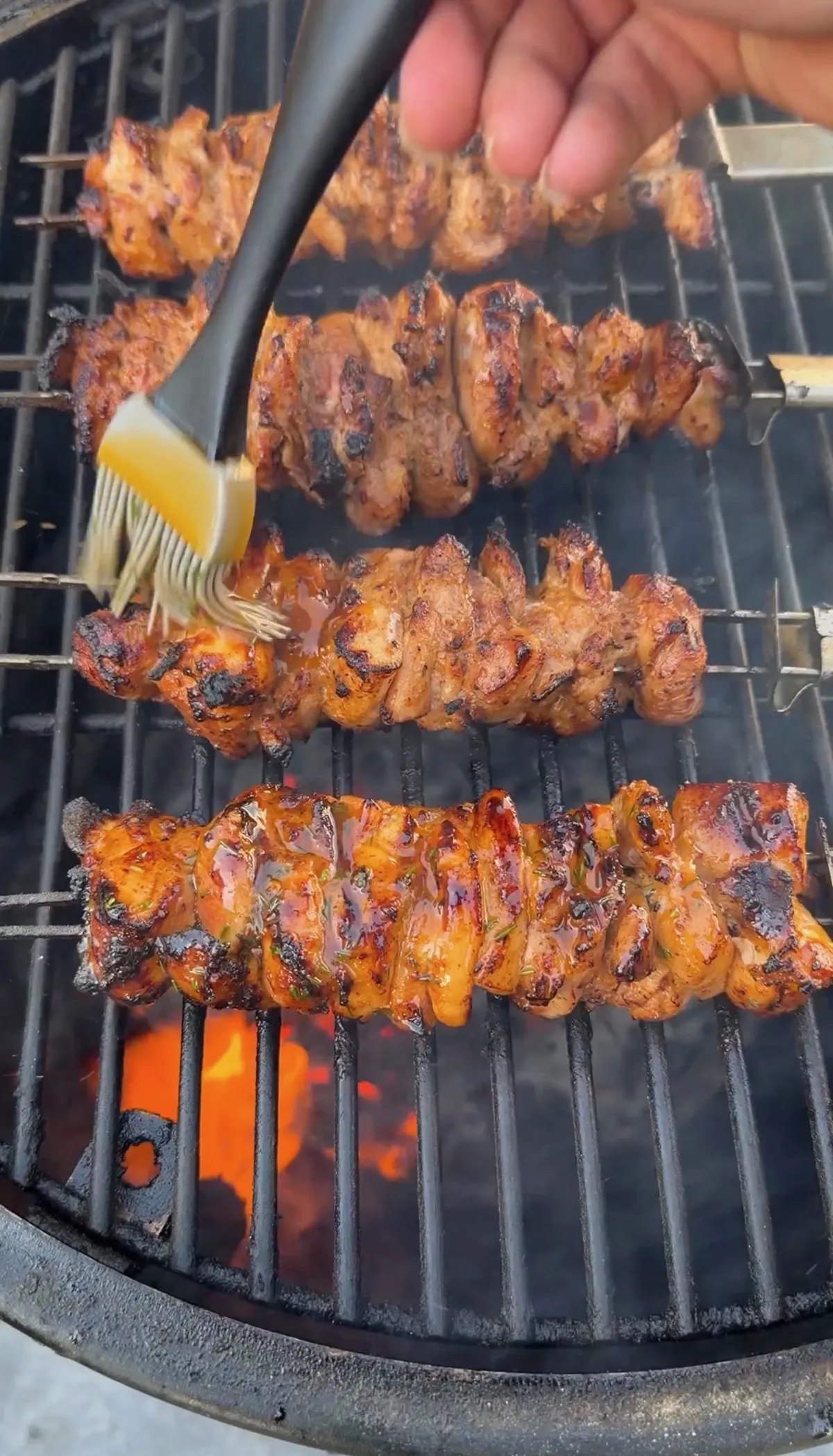 Chicken thigh skewers on charcoal grill being brushed with chili-lime glaze over open flames