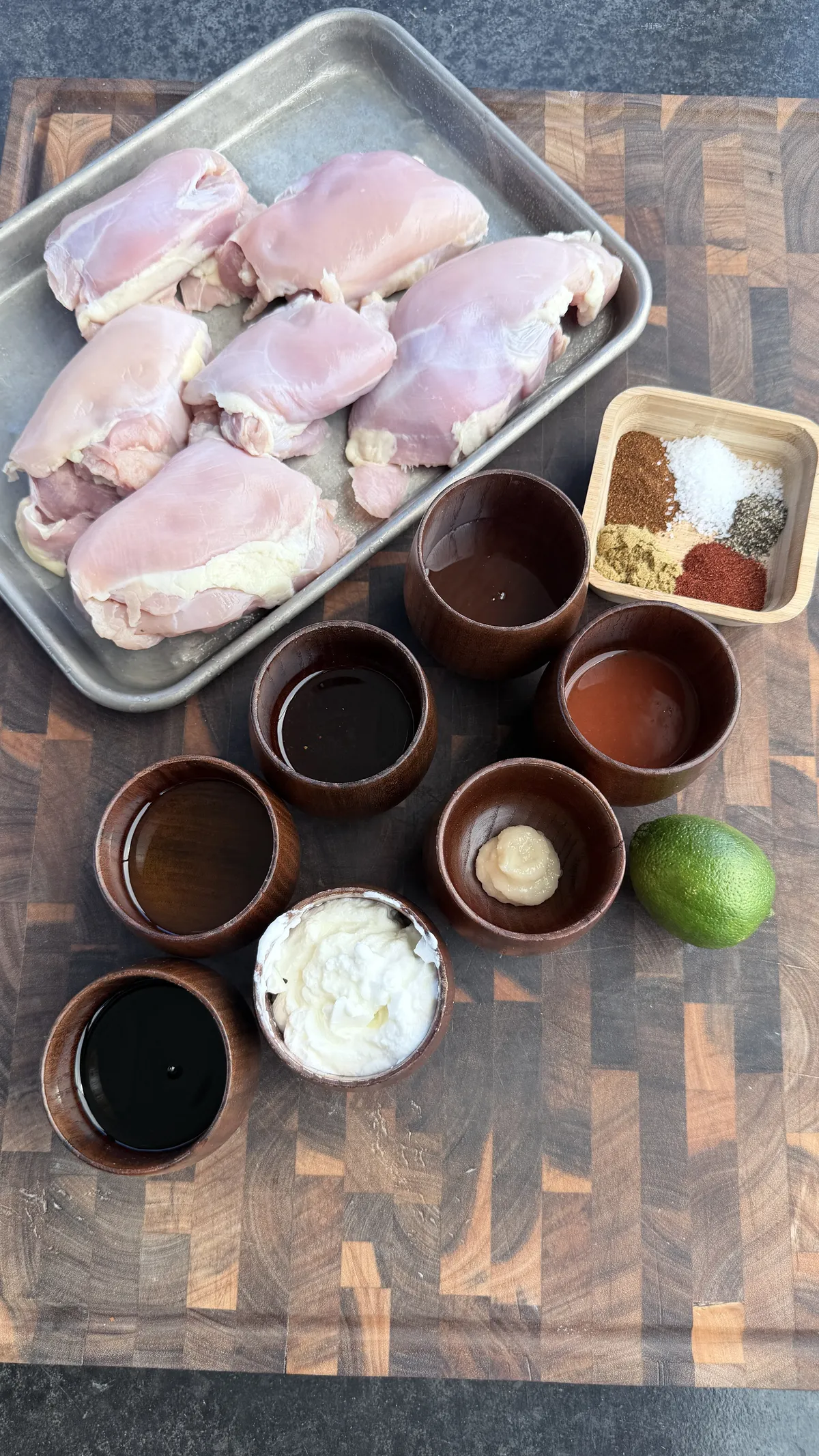 Raw boneless skinless chicken thighs with marinade ingredients: Greek yogurt, olive oil, soy sauce, honey, chili crisp, hot sauce, lime, and spices