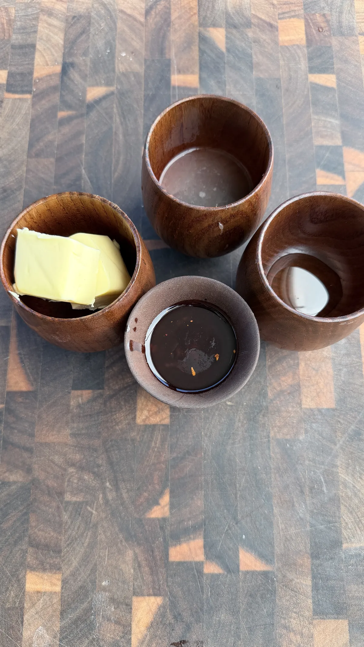 Melted butter, chili crisp, and honey in wooden cups on a cutting board for chili-lime glaze