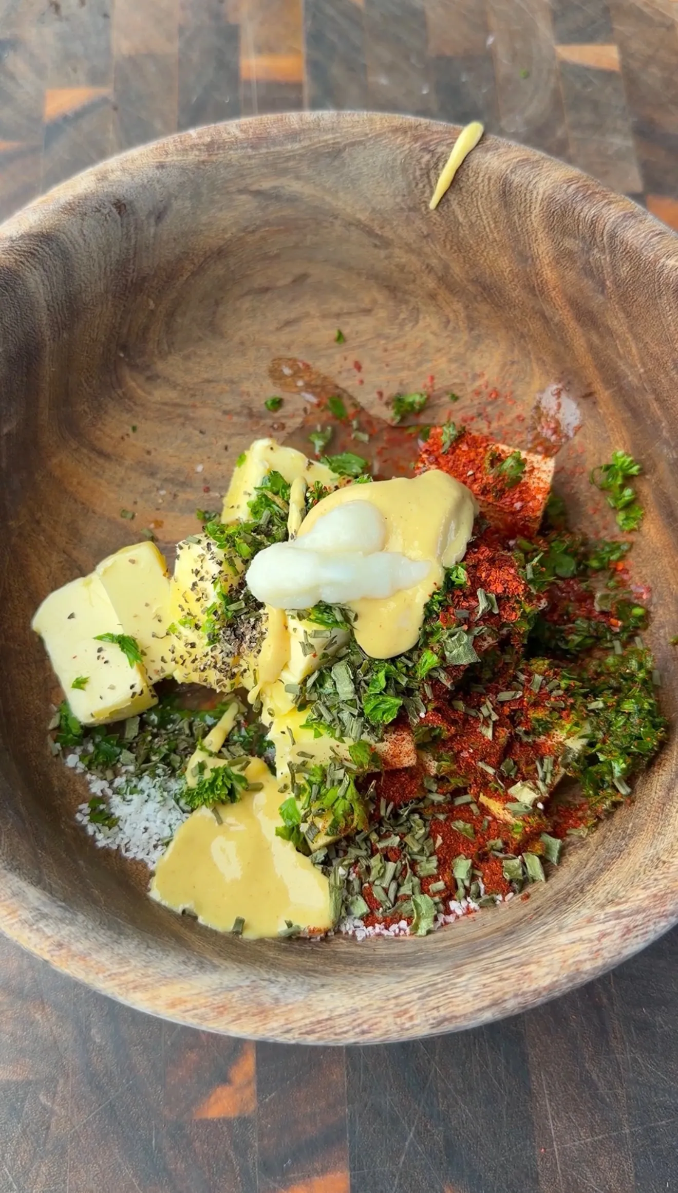 Cowboy butter ingredients in a wooden bowl: butter cubes, paprika, fresh herbs, mustard, salt, and black pepper