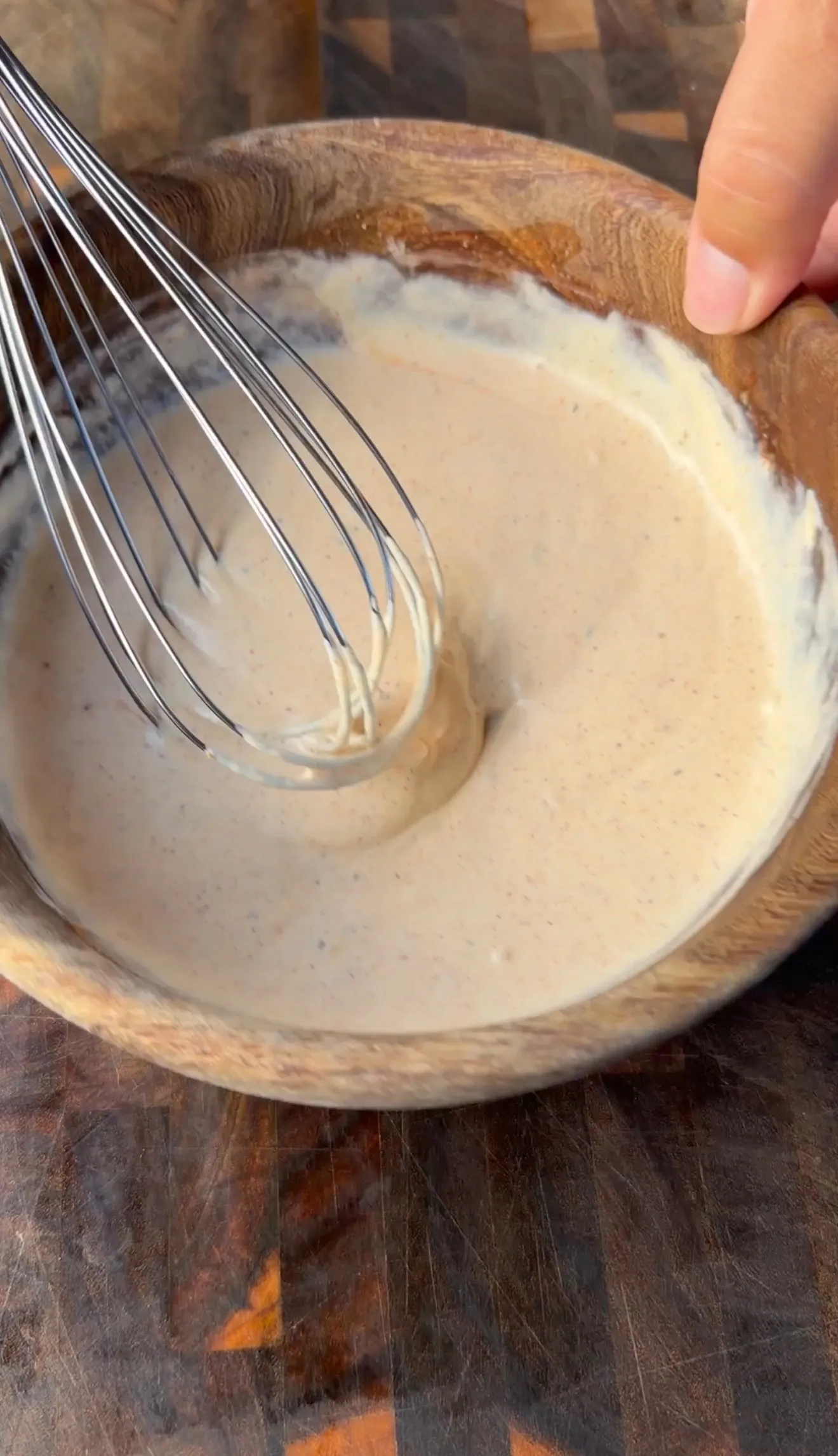 Creamy bologna sandwich sauce being whisked in a wooden bowl on a butcher block surface