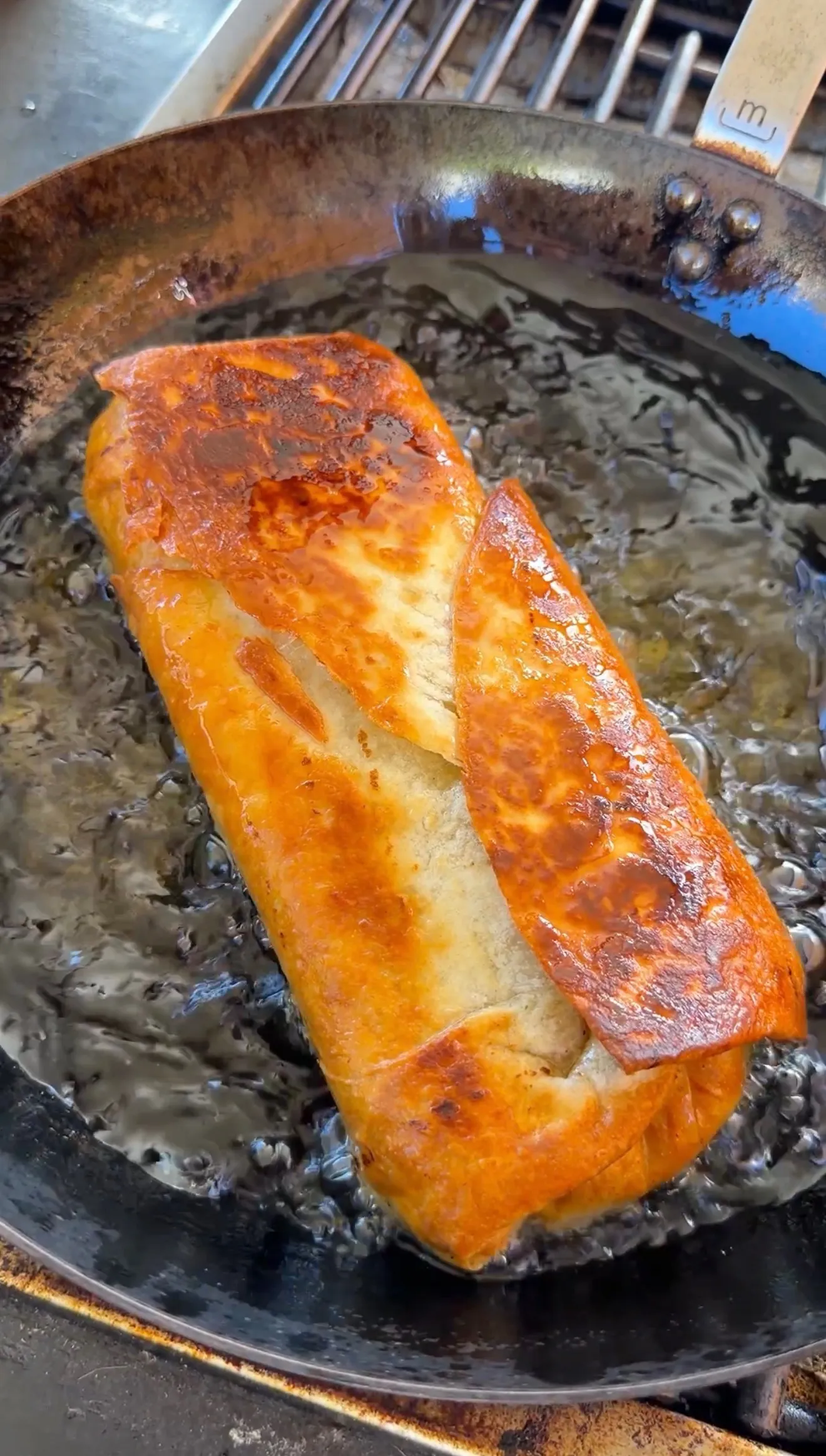 Golden-brown crispy carne asada chimichanga frying in a cast iron skillet with hot oil