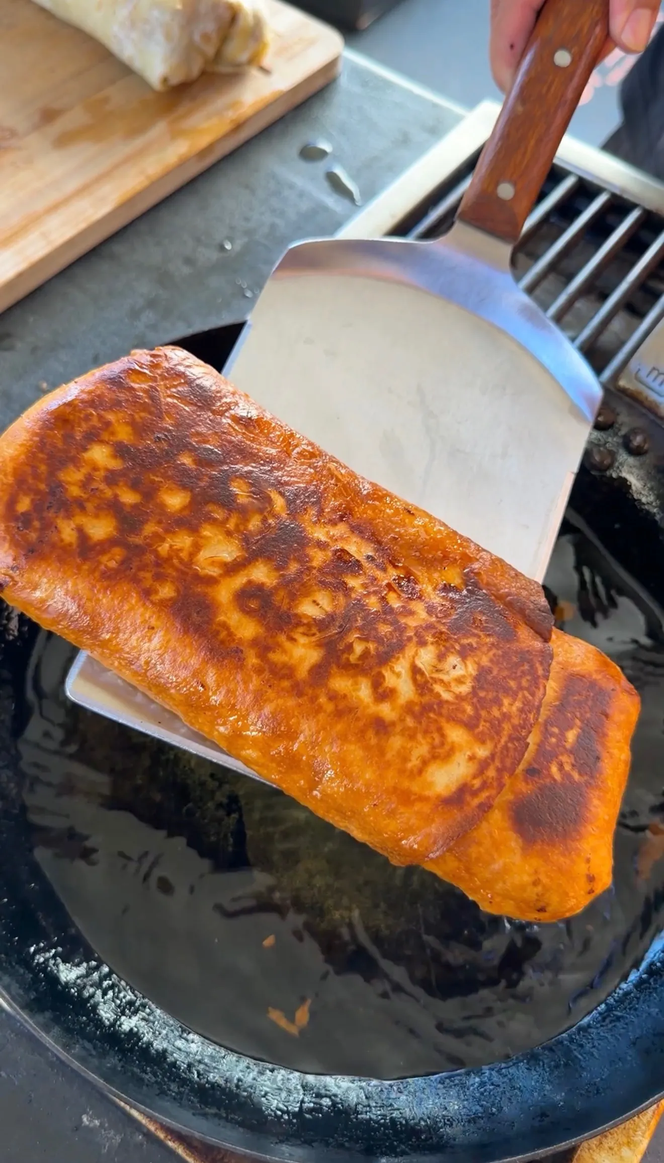 Golden-brown crispy carne asada chimichanga lifted from cast iron skillet with a spatula