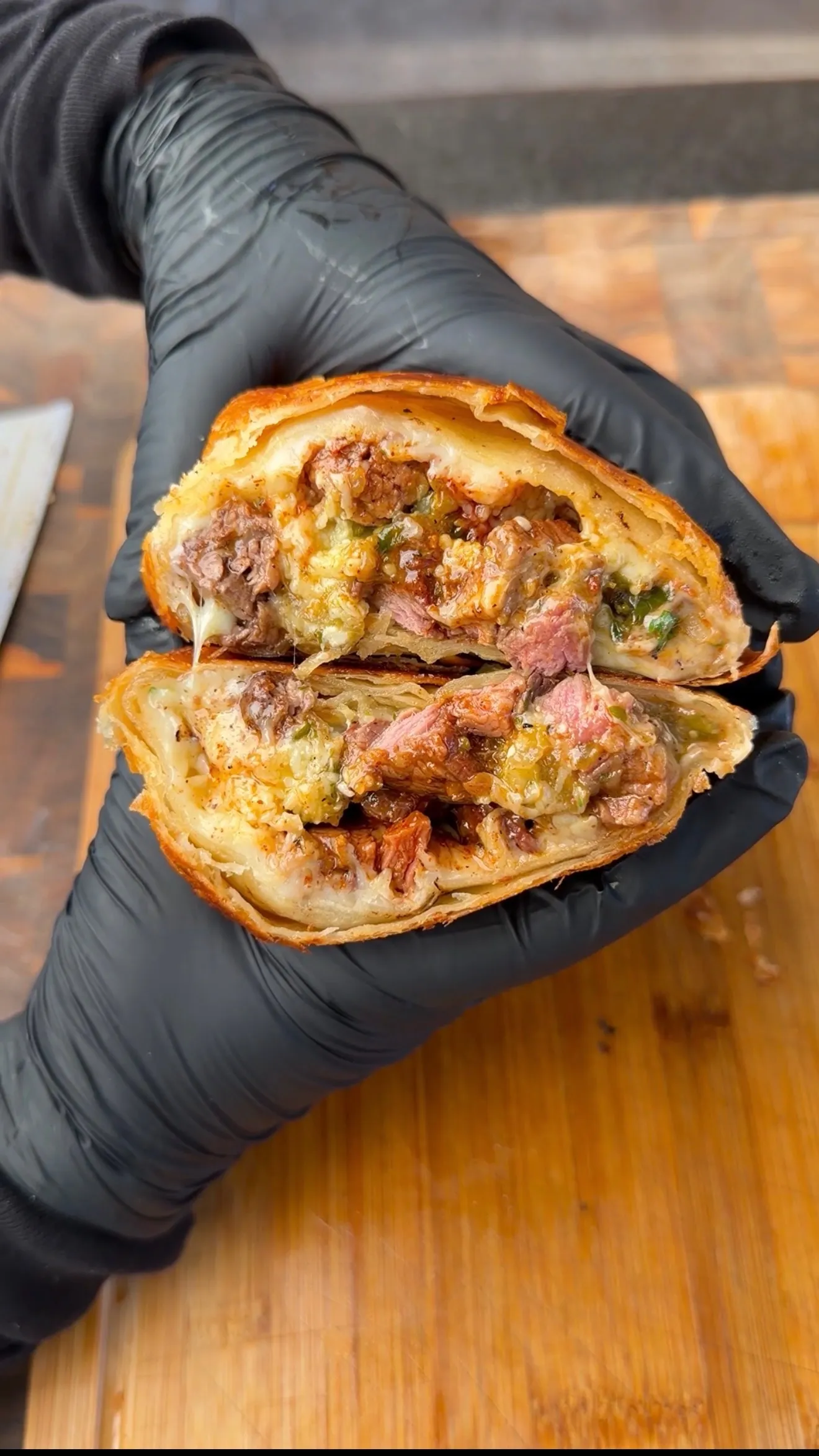 Hands holding a sliced crispy carne asada chimichanga revealing juicy steak, melted cheese, and peppers inside