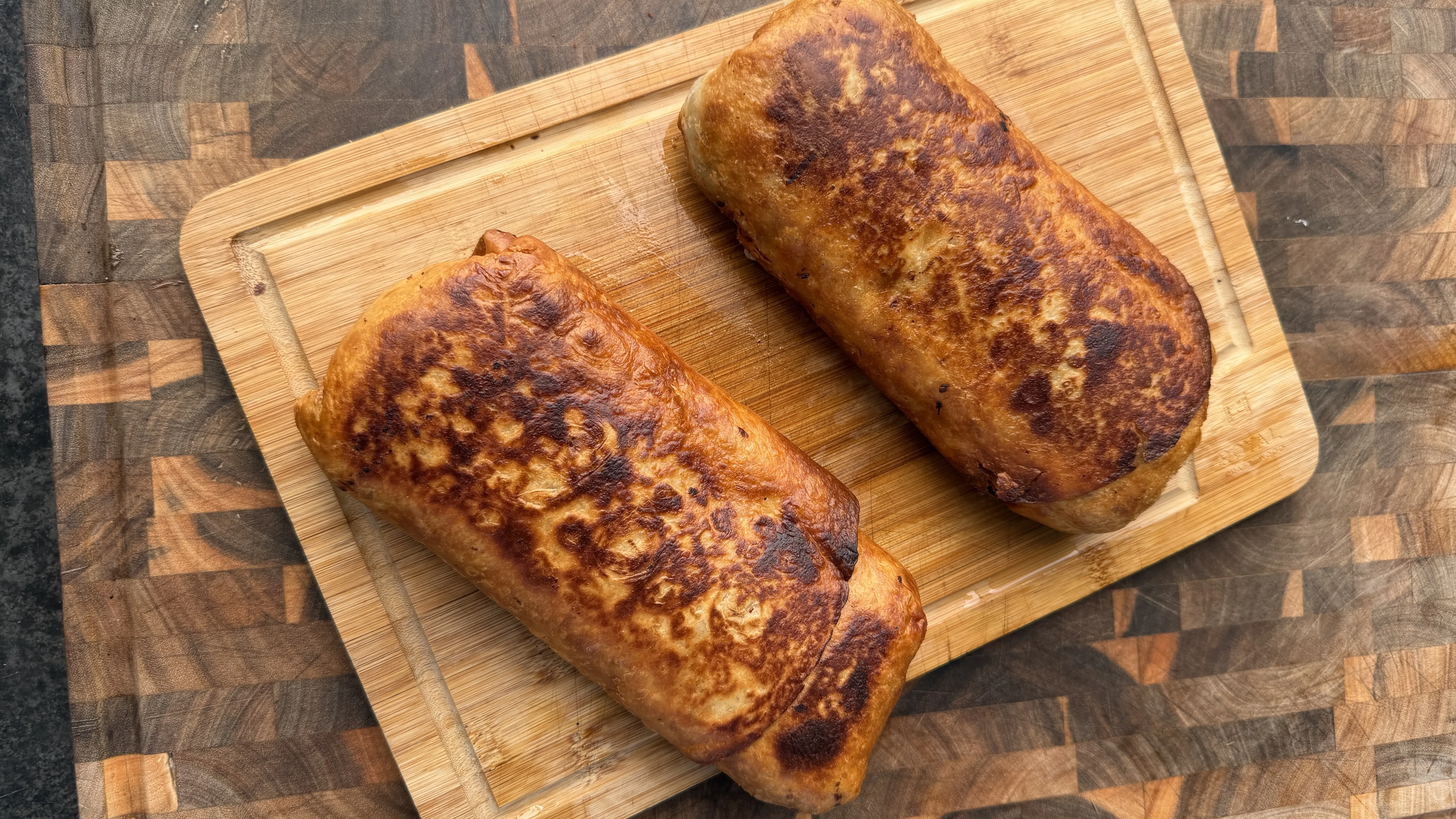 Two golden-brown crispy carne asada chimichangas with charred spots on a wooden cutting board