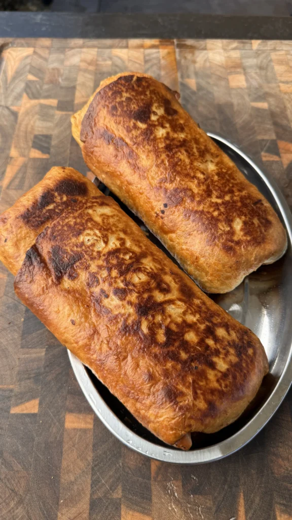 Two golden-brown crispy carne asada chimichangas on a stainless steel plate atop a wooden cutting board