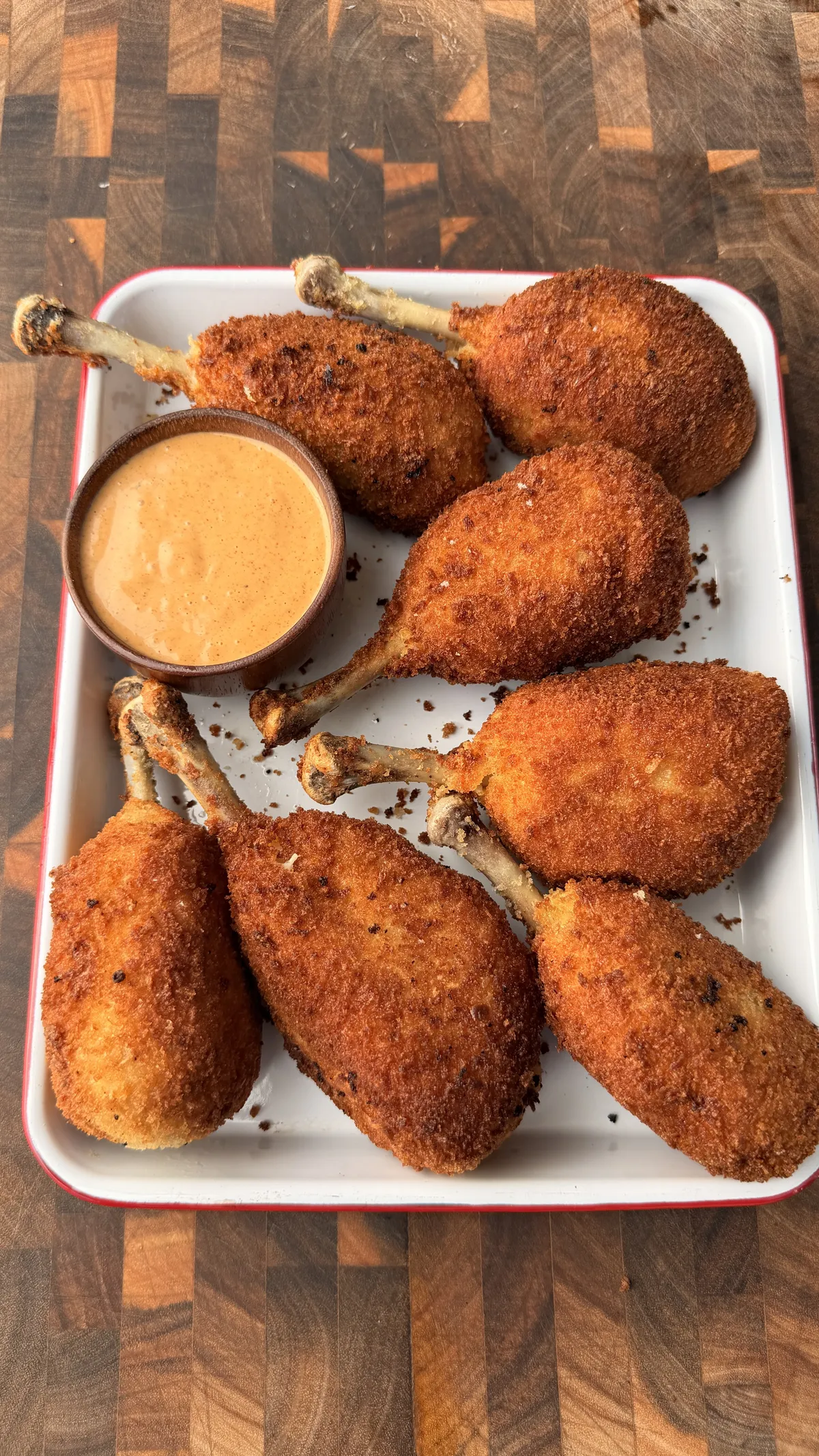 Golden panko-breaded chicken potato cheese bombs on bones served on a white tray with creamy dipping sauce