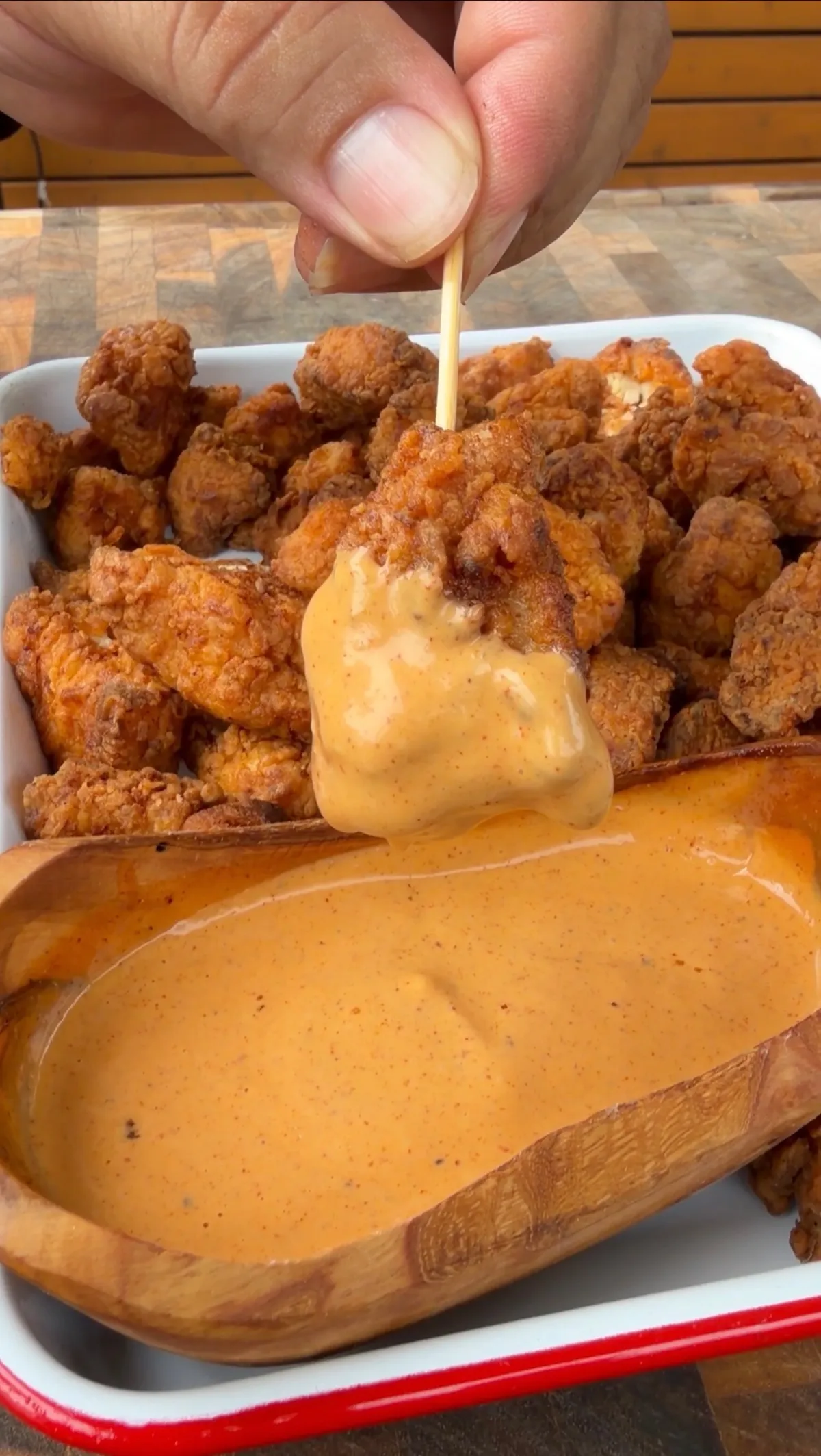 Hand dipping crispy fried popcorn chicken into a creamy spiced dipping sauce in a wooden bowl