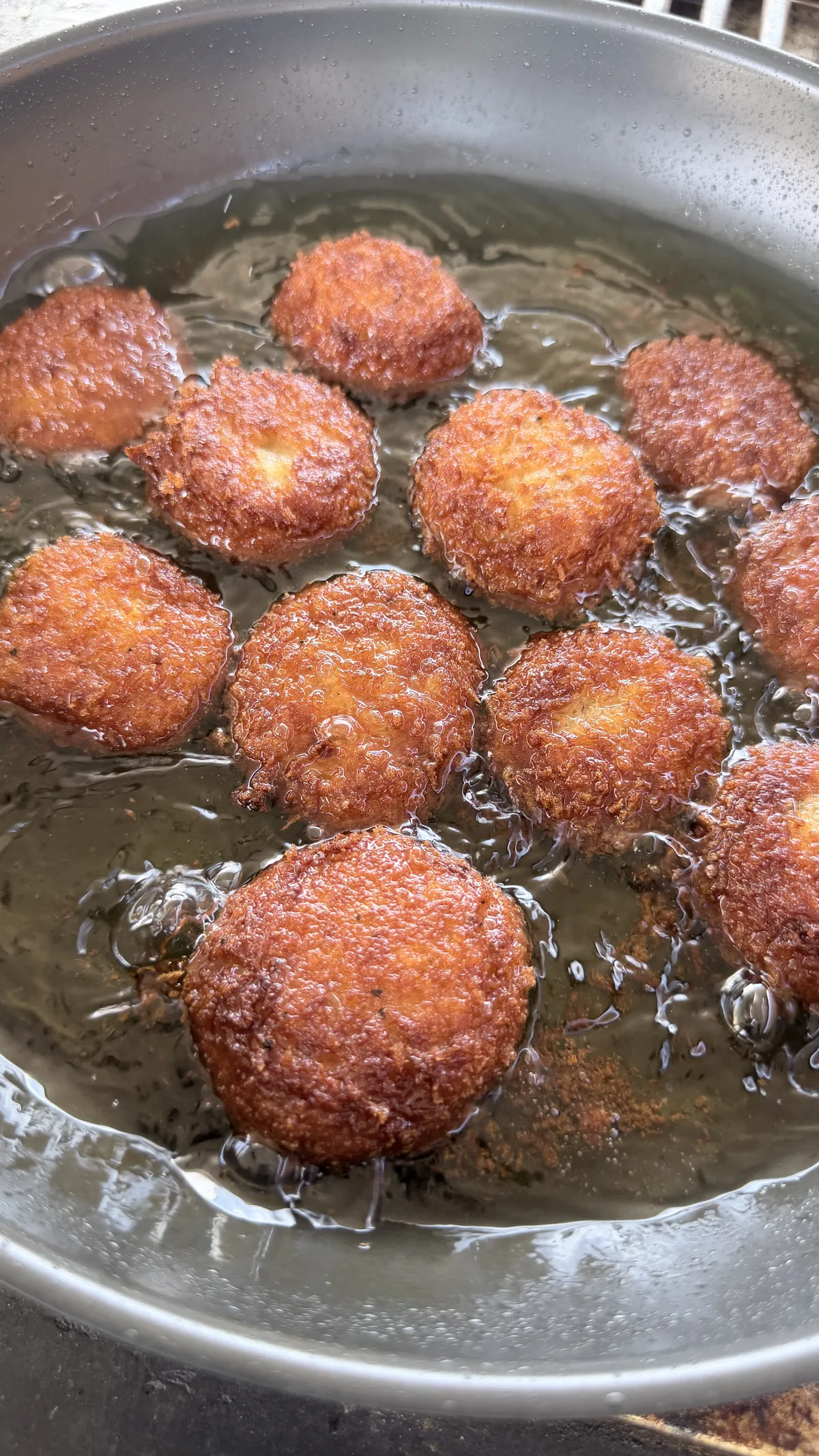 Golden crispy potato cheese balls shallow frying in hot oil in a stainless steel pan