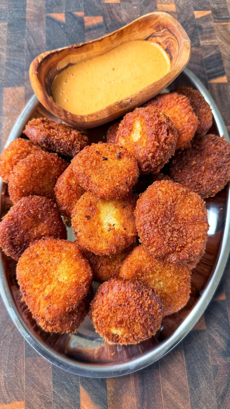 Golden crispy potato cheese balls piled in a silver tray with creamy orange dipping sauce in a wooden bowl