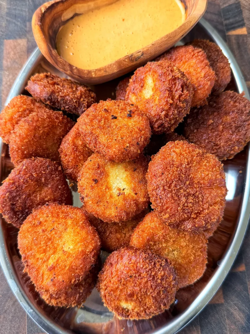 Golden crispy potato cheese balls piled in a silver tray with creamy orange dipping sauce in a wooden bowl