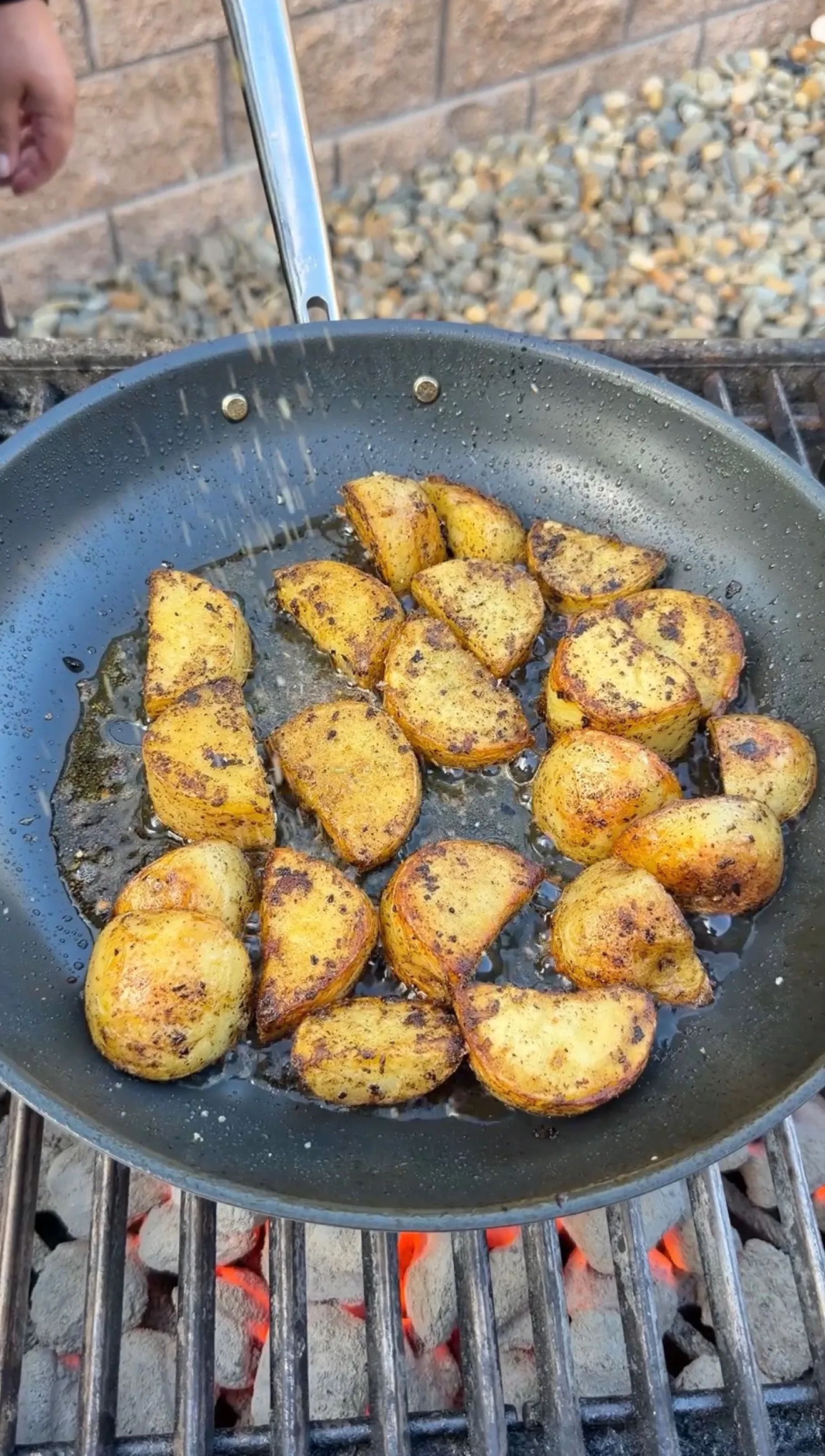 Seasoned crispy potato wedges sizzling in a dark skillet over hot charcoal grill grates outdoors