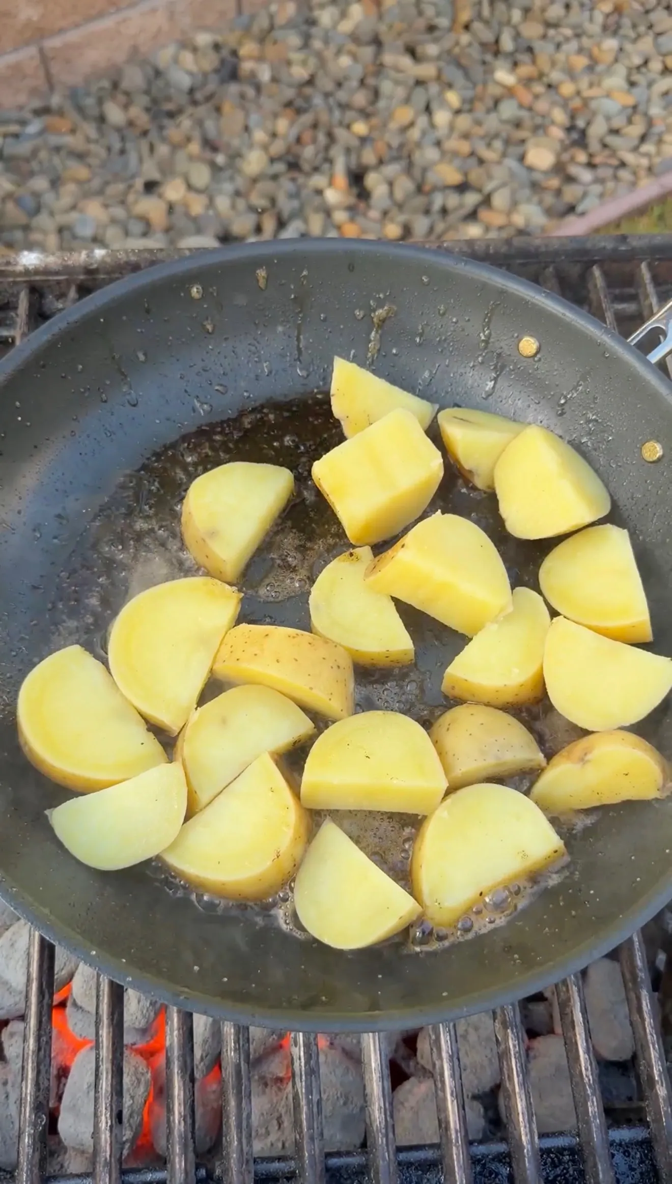Diced yellow potatoes sizzling in a dark skillet over an open flame grill, cooking for crispy potatoes