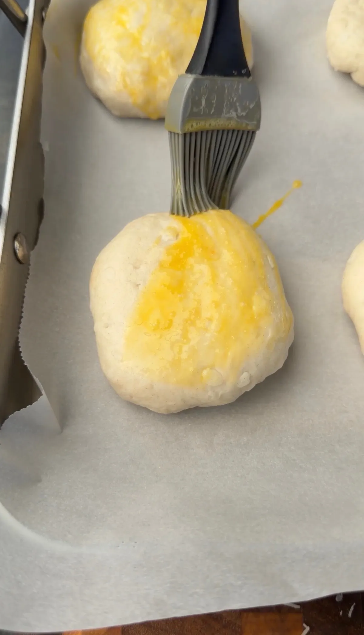Silicone pastry brush applying egg wash to raw pizza bomb dough balls on parchment-lined baking sheet
