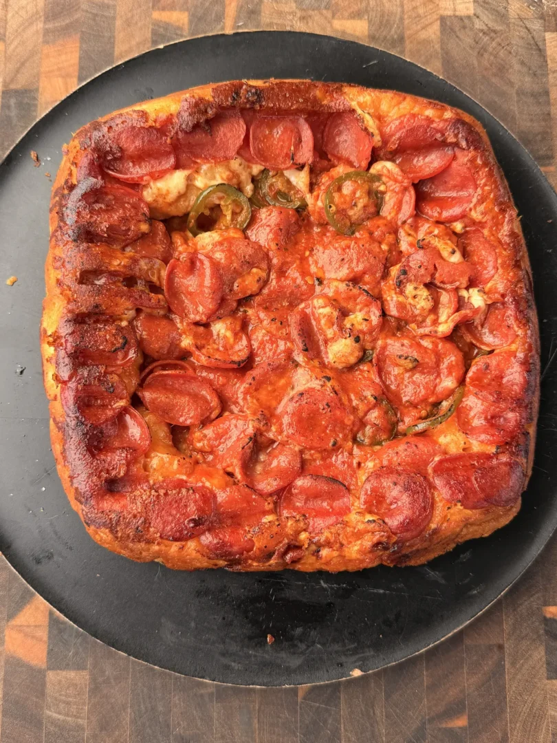 Upside-down deep dish pepperoni pizza with jalapeño slices and melted mozzarella on a black round pan