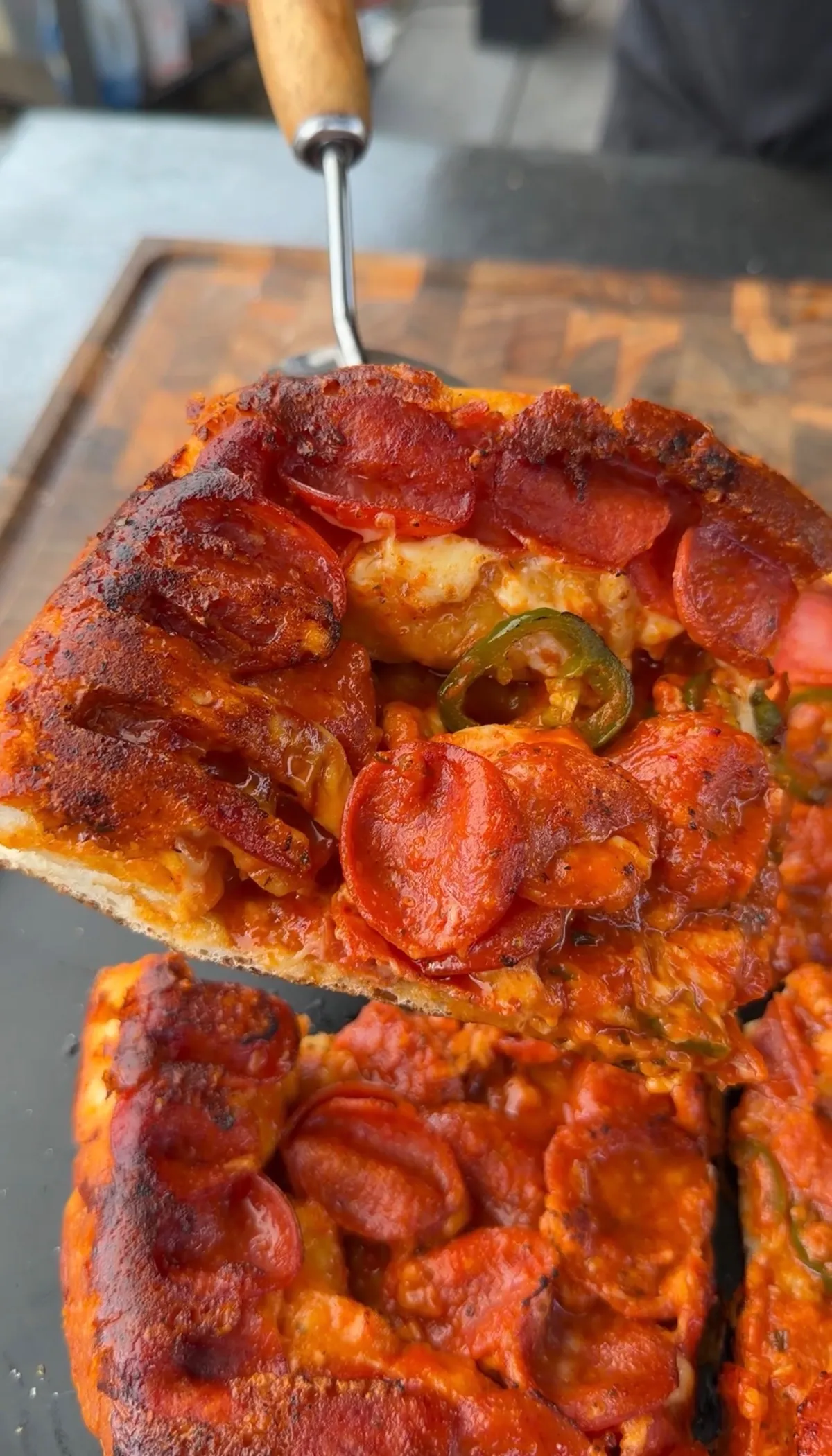 Slice of upside-down deep dish pizza lifted by spatula, showing crispy pepperoni, melted mozzarella, and fresh jalapeño rounds on top