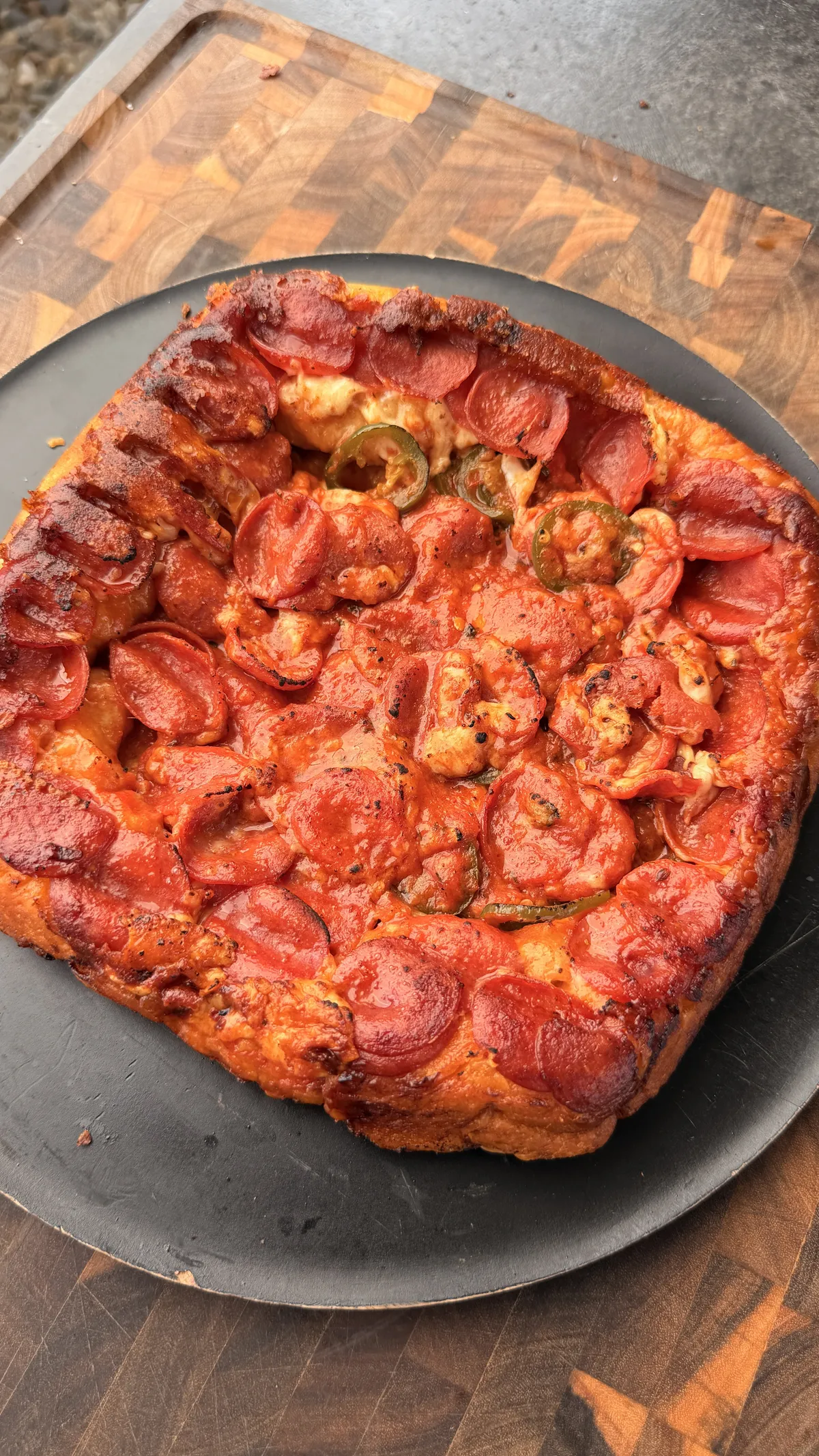 Upside-down deep dish pepperoni pizza with jalapeño slices and melted mozzarella on a dark round pan
