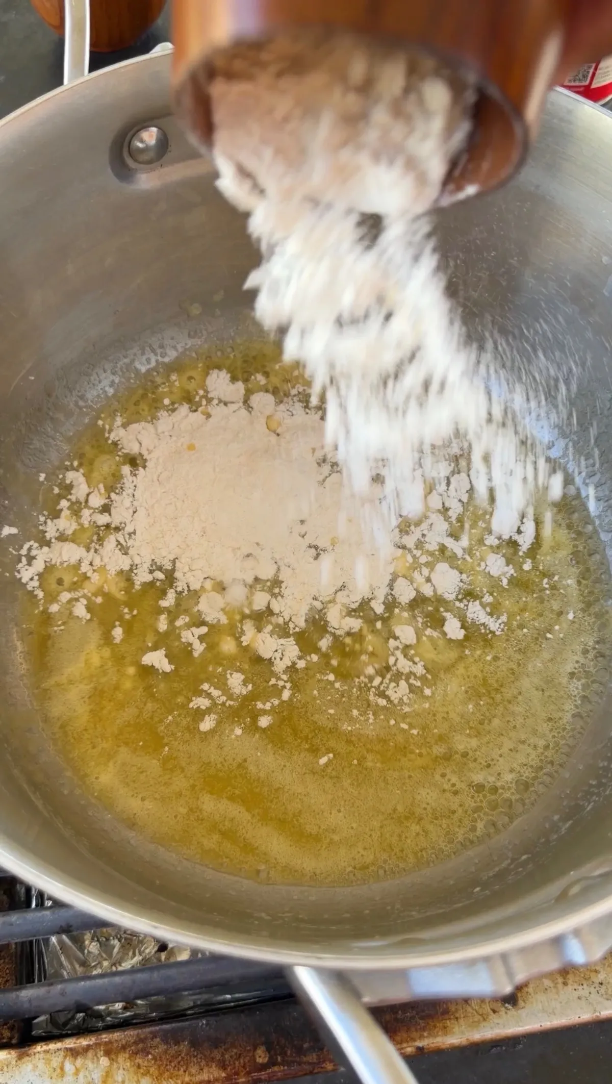 All-purpose flour being poured into melted butter in a stainless steel pan to make a roux for mac and cheese