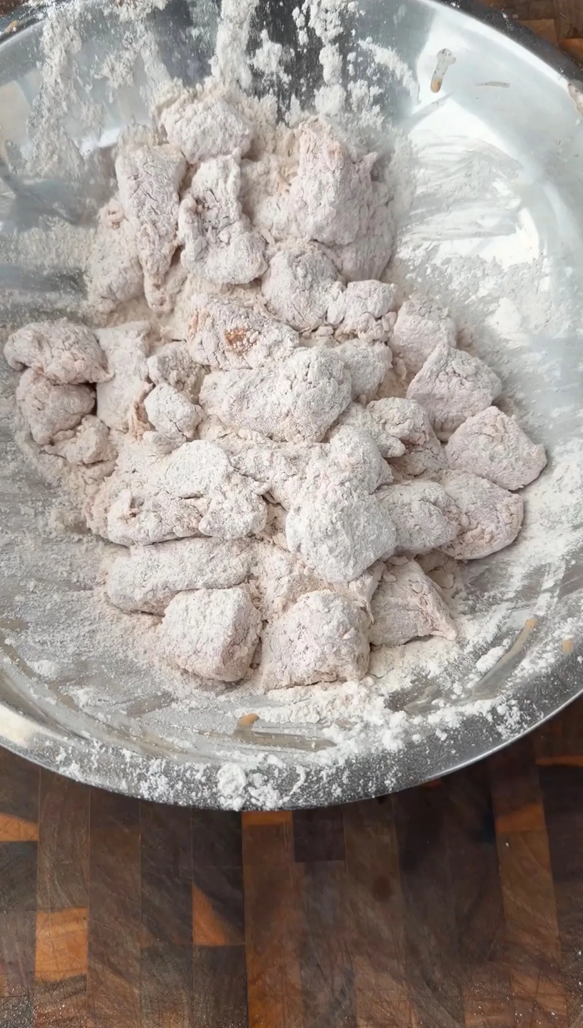 Raw chicken pieces thoroughly coated in seasoned flour in a stainless steel mixing bowl, ready for frying