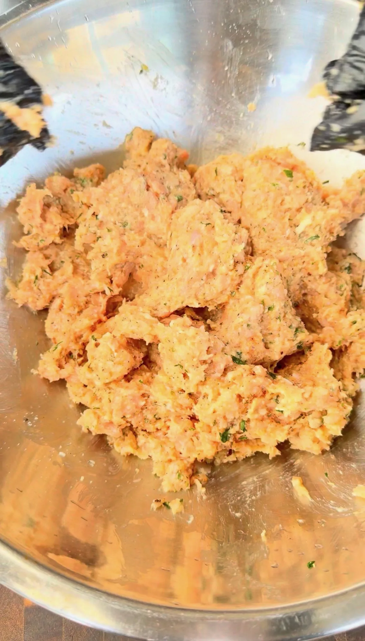 Seasoned ground chicken mixture with garlic, parmesan, and herbs in a stainless steel mixing bowl