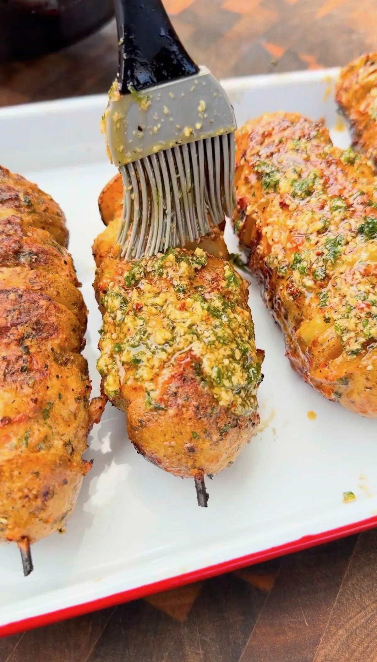 Garlic parmesan chicken and potato skewers being brushed with herb butter glaze on a white serving tray