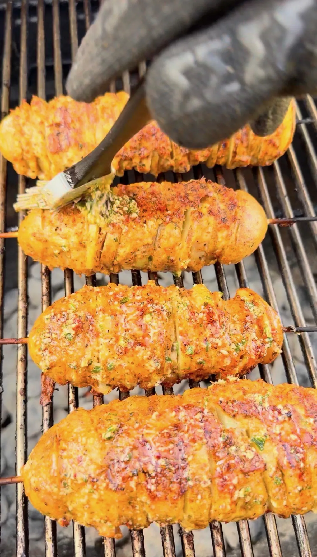Garlic parmesan chicken and potato skewers on a charcoal grill being basted with herb butter sauce