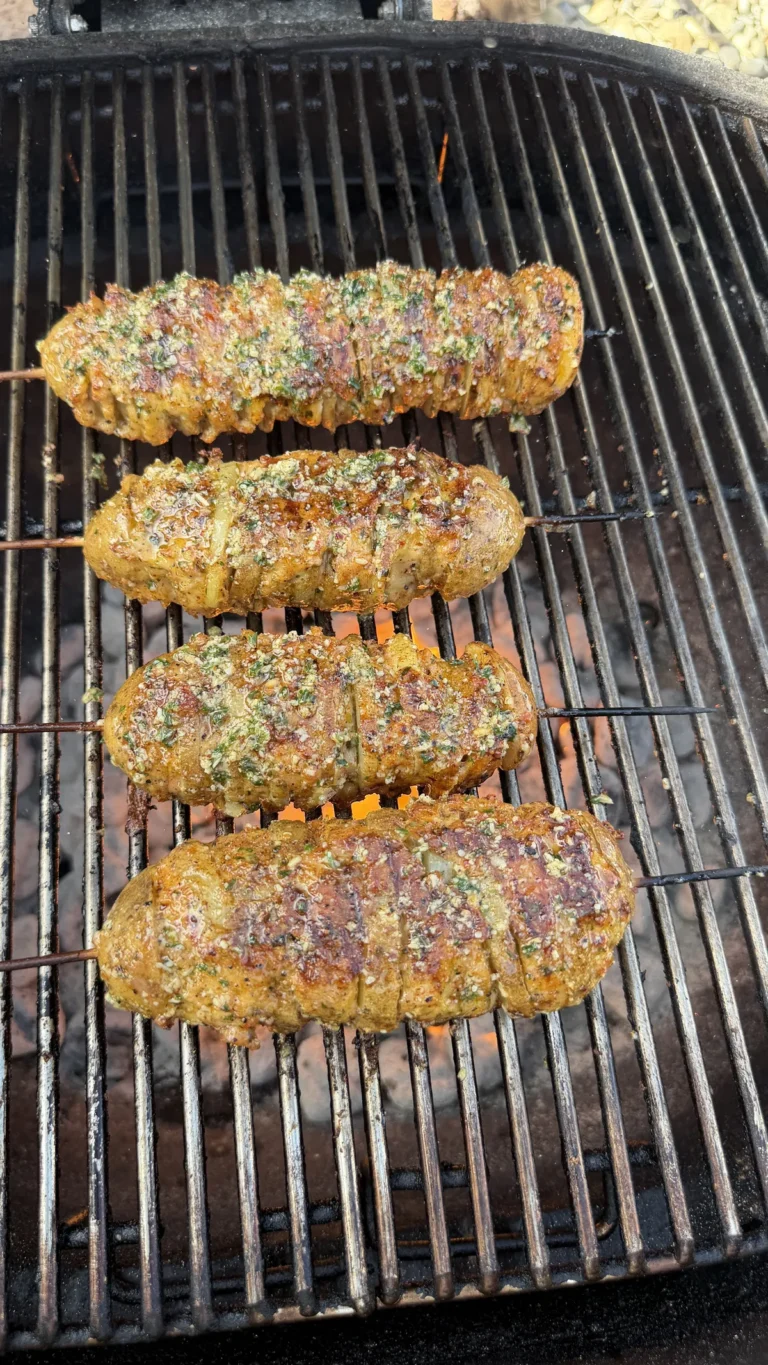 Four garlic parmesan chicken and potato skewers grilling over open flame on a charcoal grill