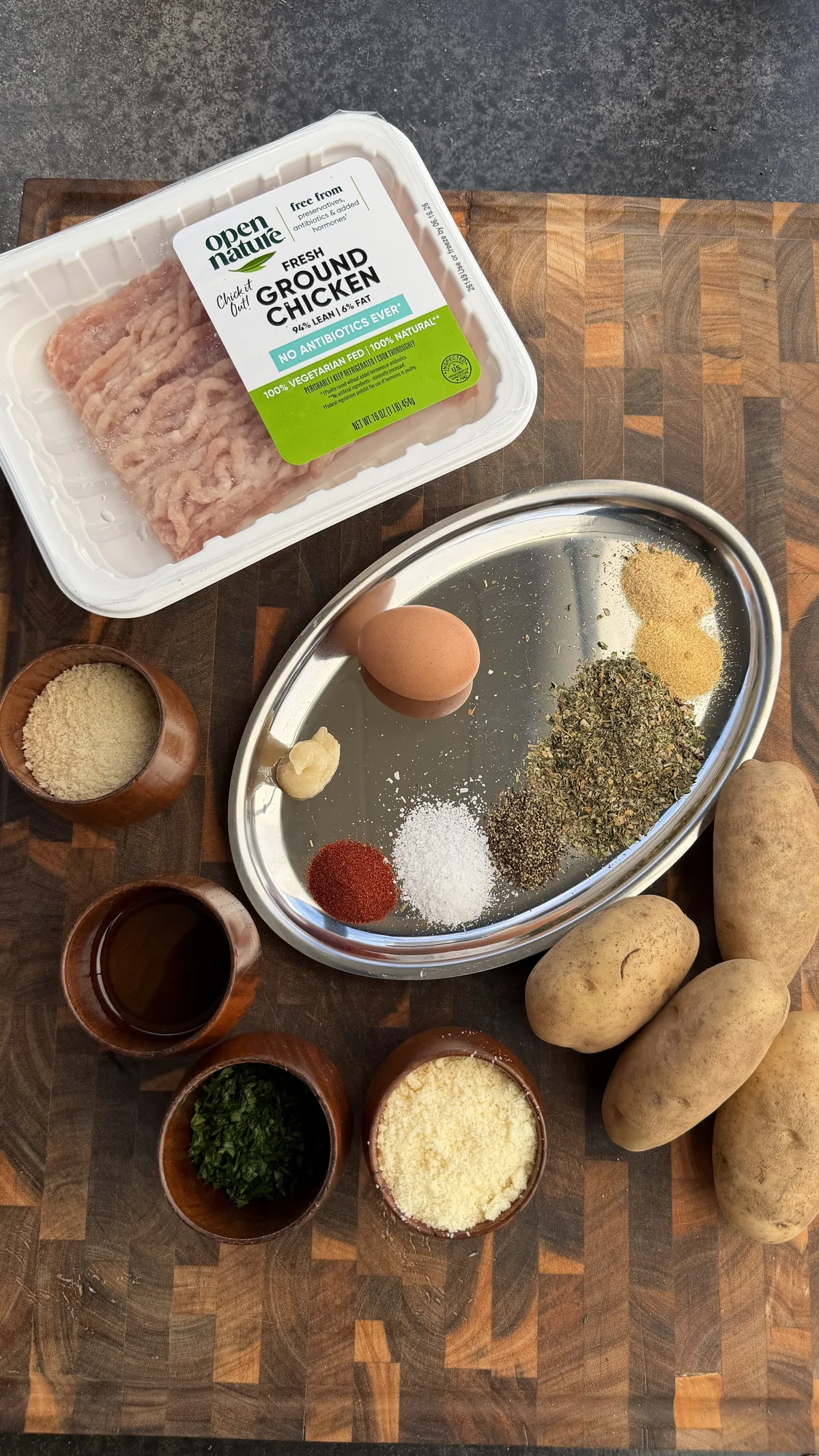 Ingredients for garlic parmesan chicken potato skewers including ground chicken, spices, egg, potatoes, and parmesan on cutting board