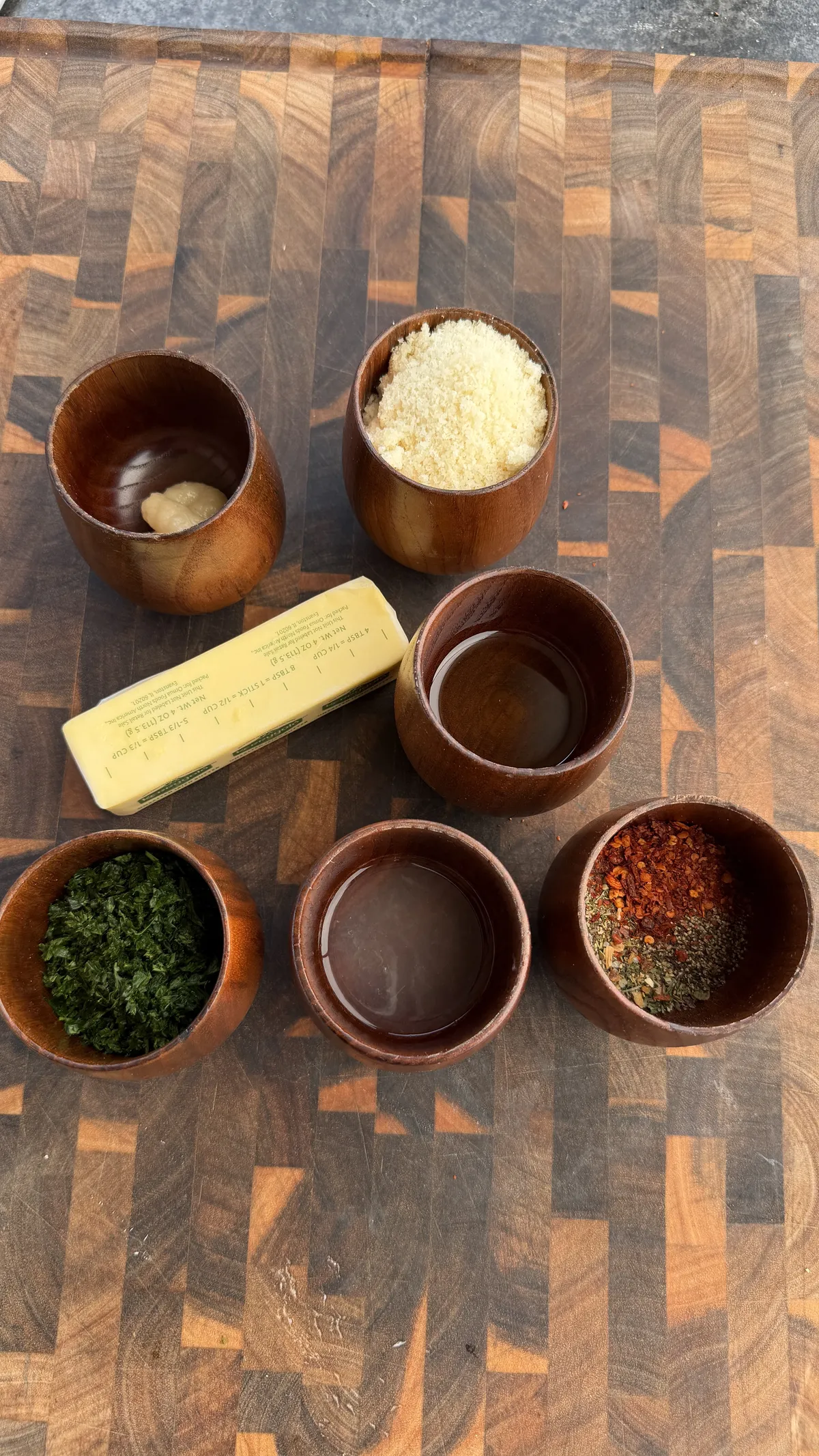 Wooden bowls with garlic, parmesan, herbs, spices, oil, and a butter stick for garlic parmesan chicken skewers