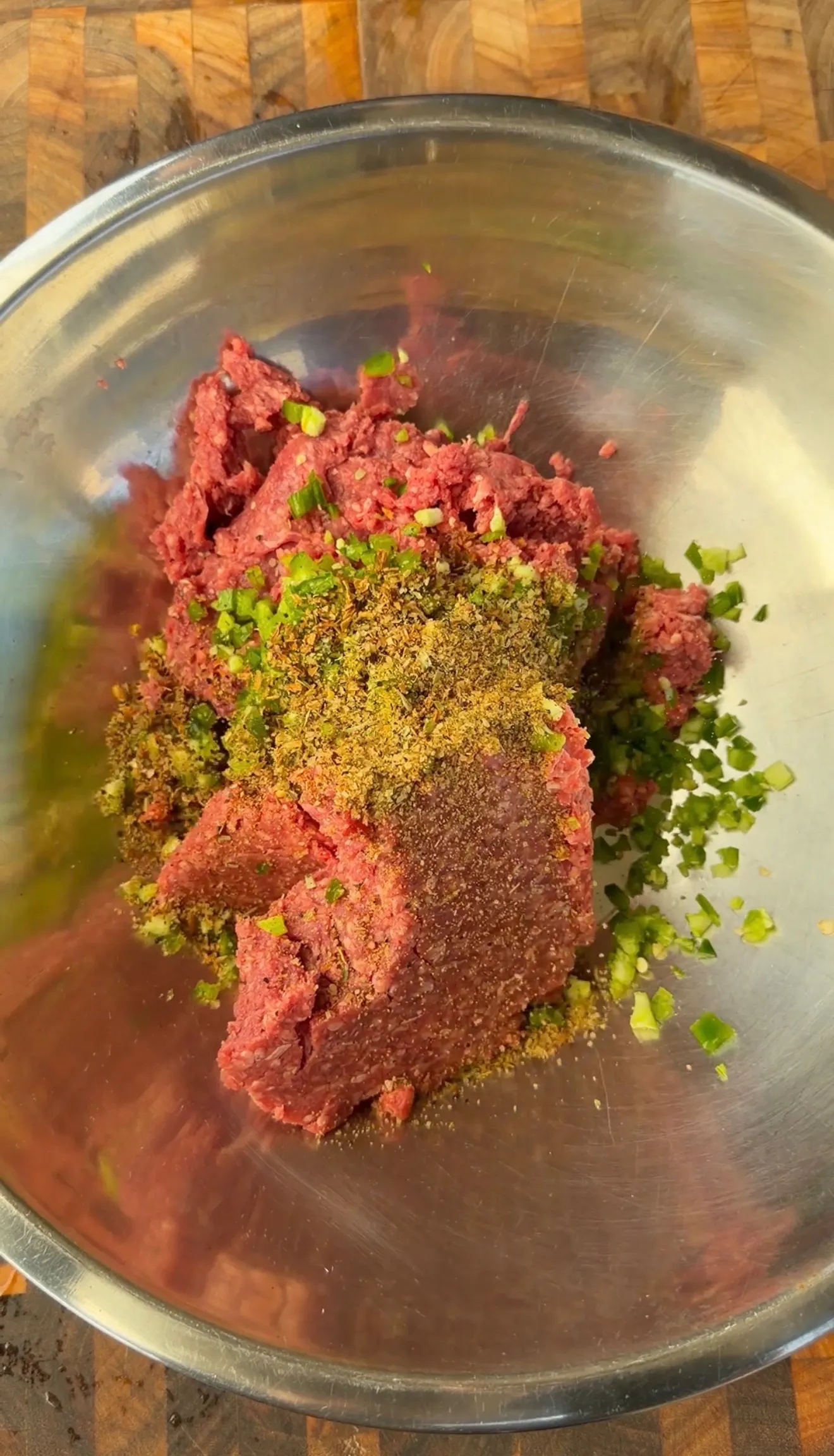 Raw ground beef mixed with diced jalapeños and spices in a stainless steel mixing bowl for burger dogs