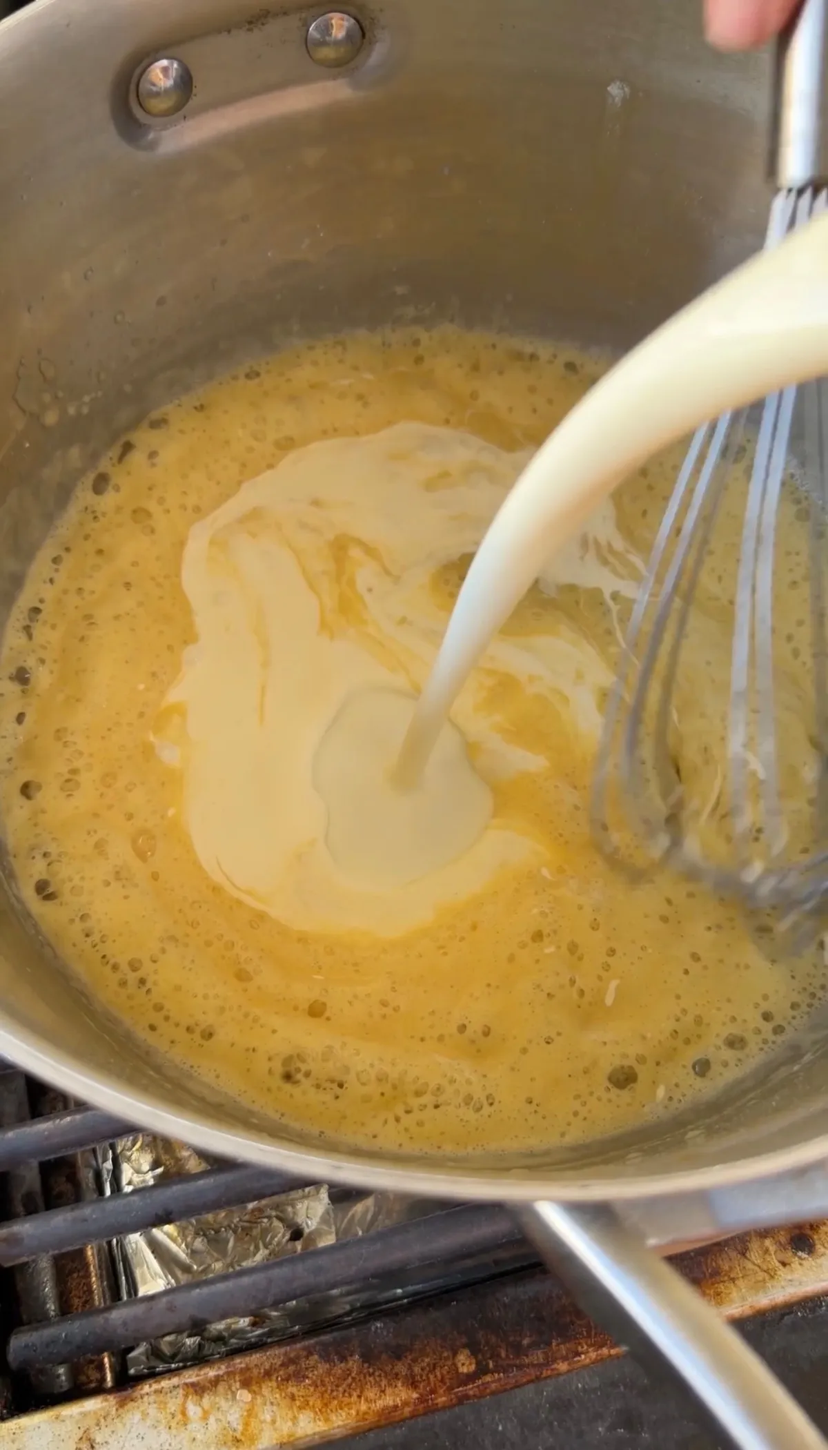 Heavy whipping cream and evaporated milk being whisked into a golden roux in a stainless steel pot on the stove