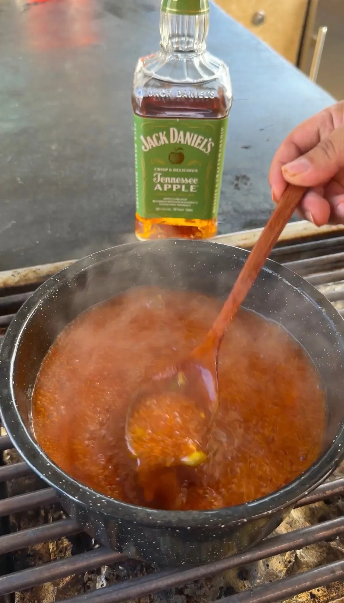 Jack Daniel's Tennessee Apple whiskey BBQ sauce bubbling in a pan on a grill, stirred with a wooden spoon