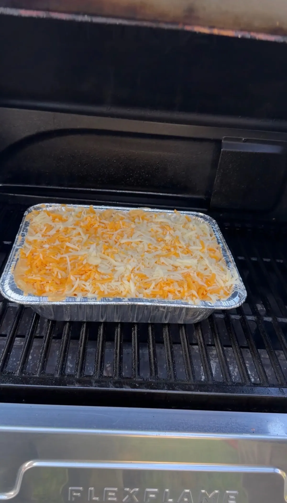 Elbow macaroni and cheese topped with shredded Colby Jack and mozzarella in a foil pan on a grill at 400°F